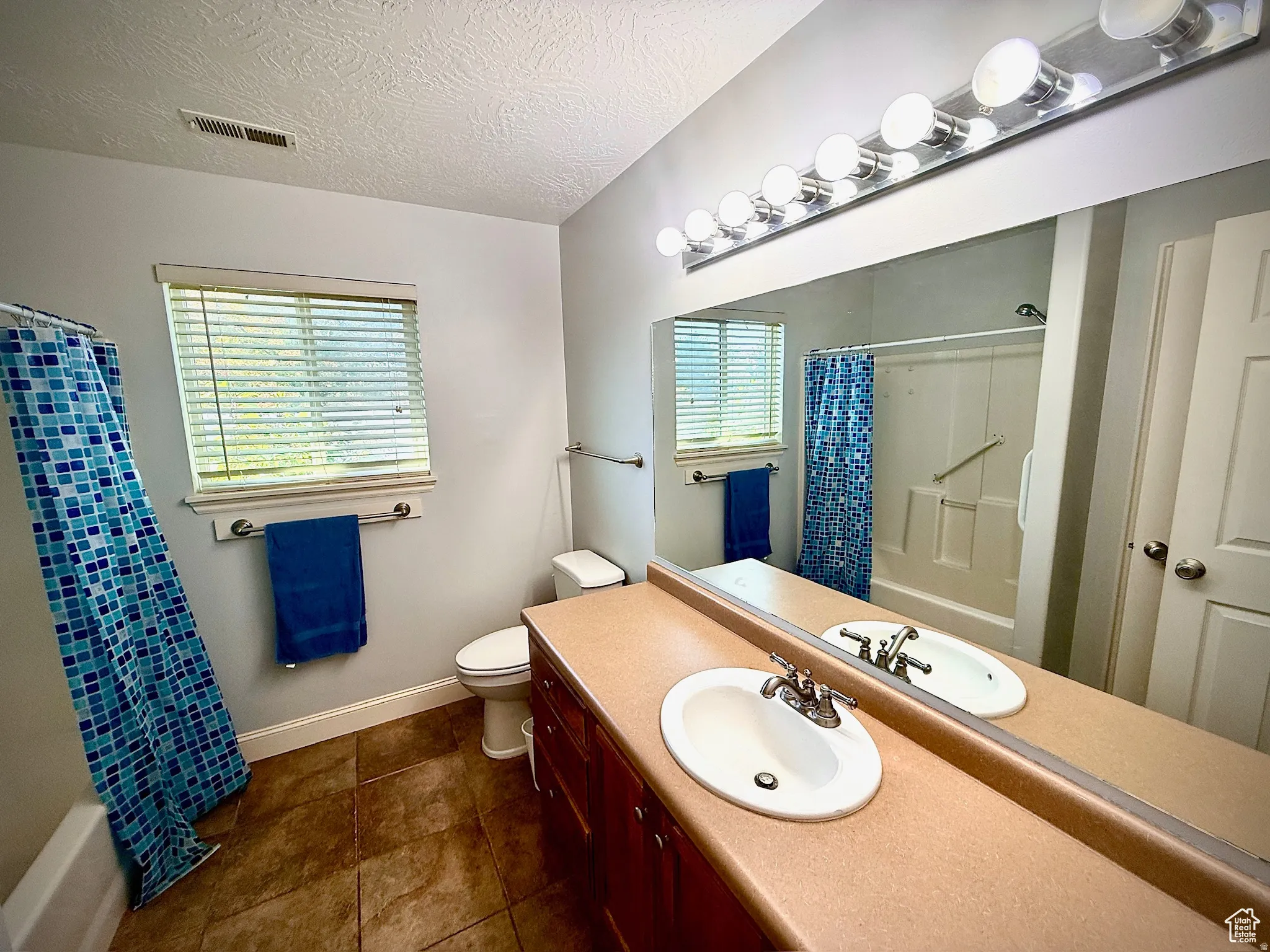 Bathroom featuring vanity, a textured ceiling, dark tile patterned flooring, and shower / tub combo with curtain