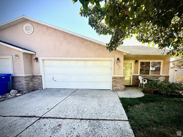 Single story home featuring stucco siding, an attached garage, driveway, and stone siding