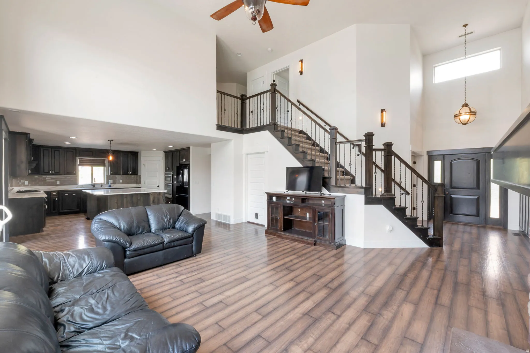 Spacious open-concept living area featuring wood-finish flooring and a two-story ceiling with a ceiling fan
