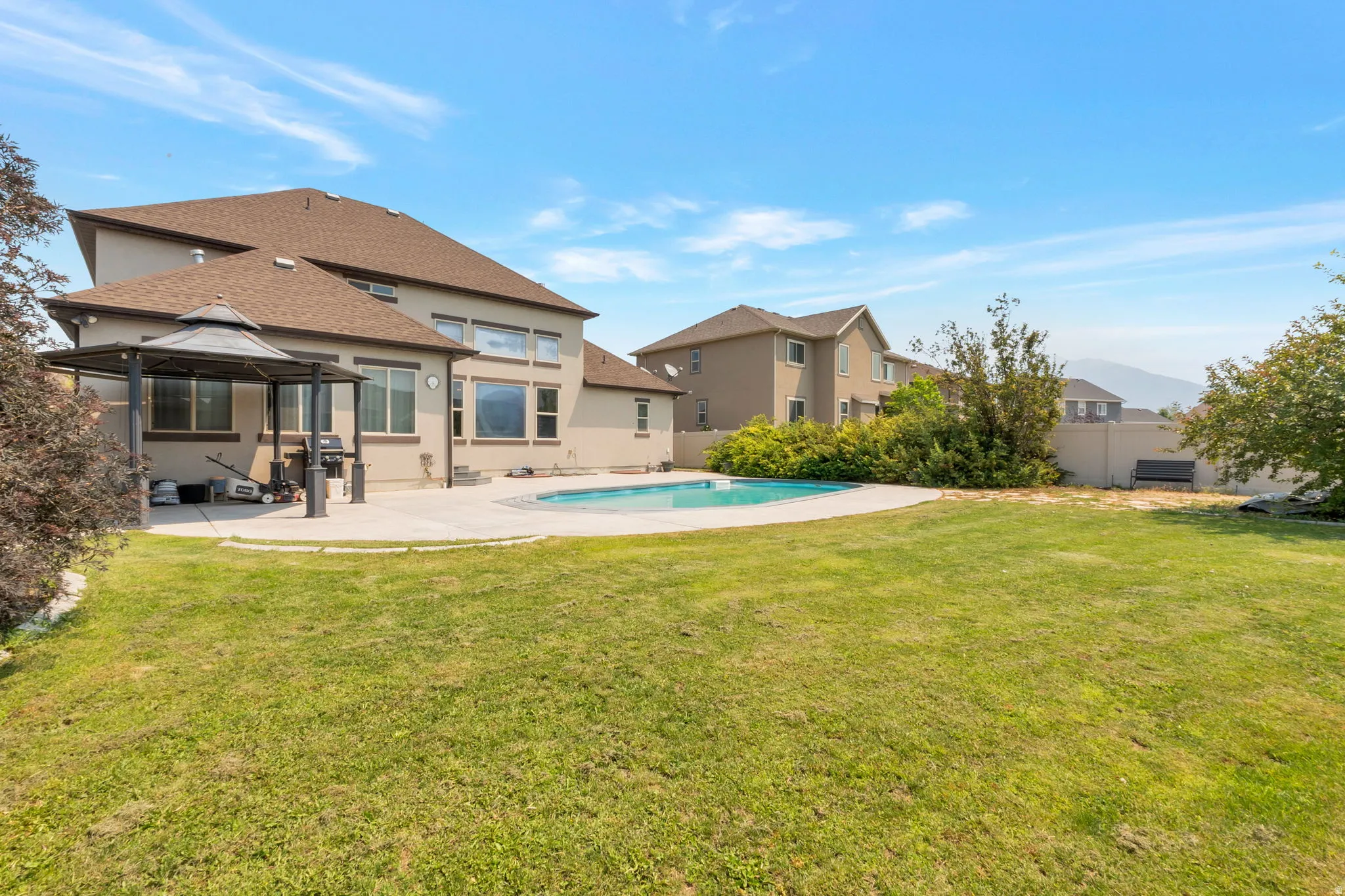 Expansive backyard featuring a large in-ground swimming pool with a concrete surround, a covered gazebo, a stucco exterior, and a visible distant mountain range