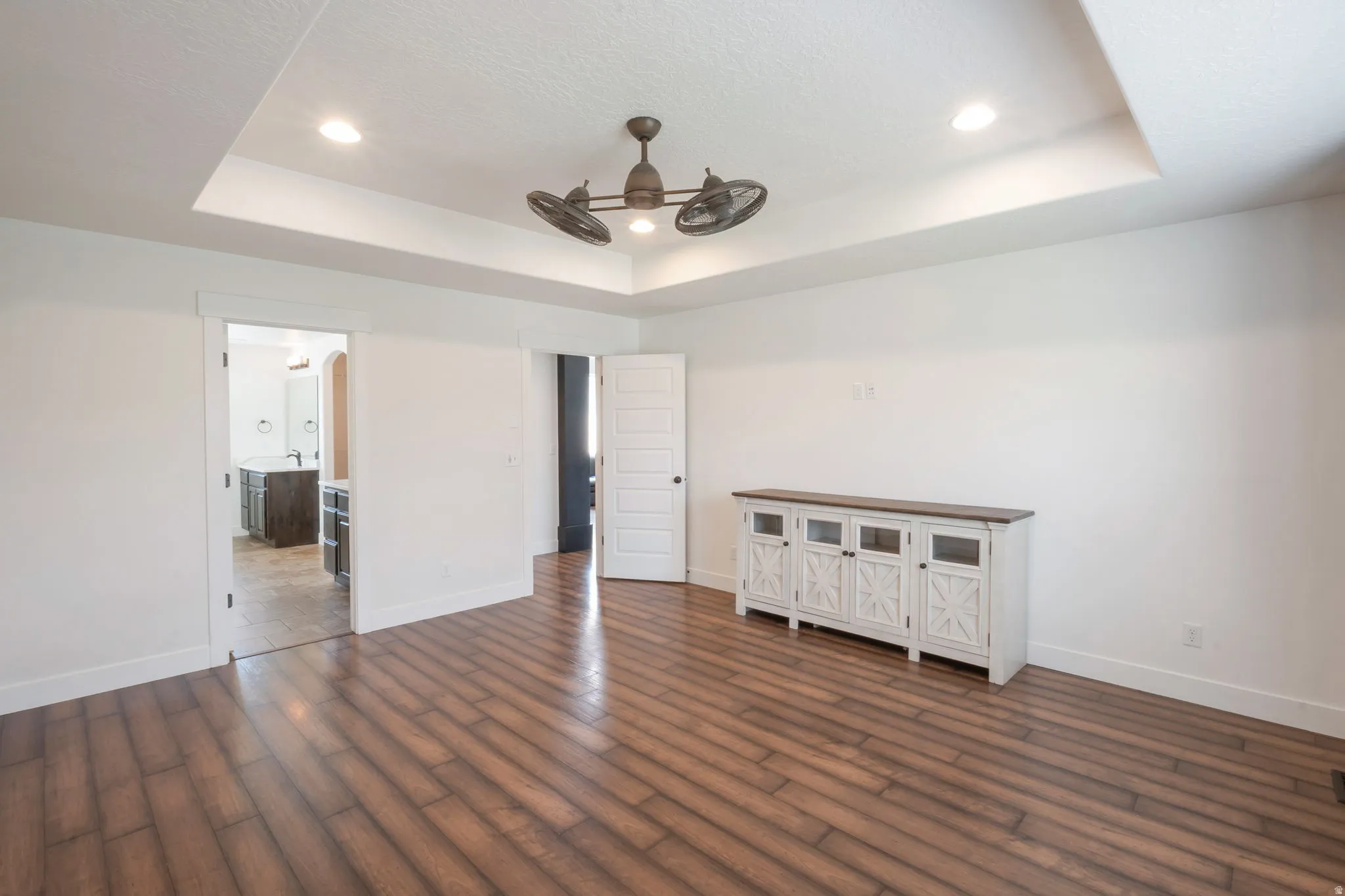 Spacious interior featuring wood-finish flooring, a tray ceiling with recessed lighting, and a ceiling fan