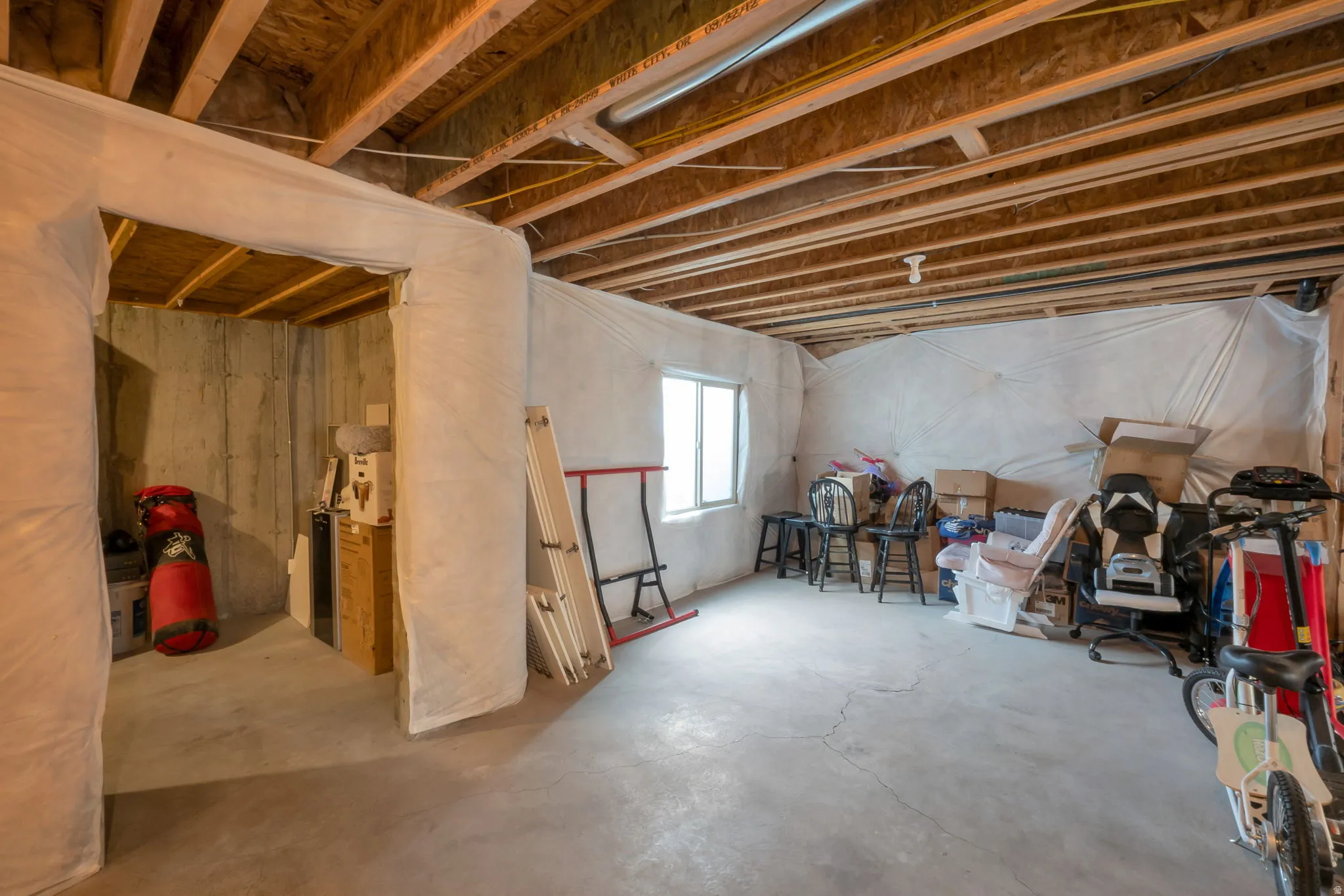 Unfinished basement featuring exposed wood joists, concrete flooring, and a single window