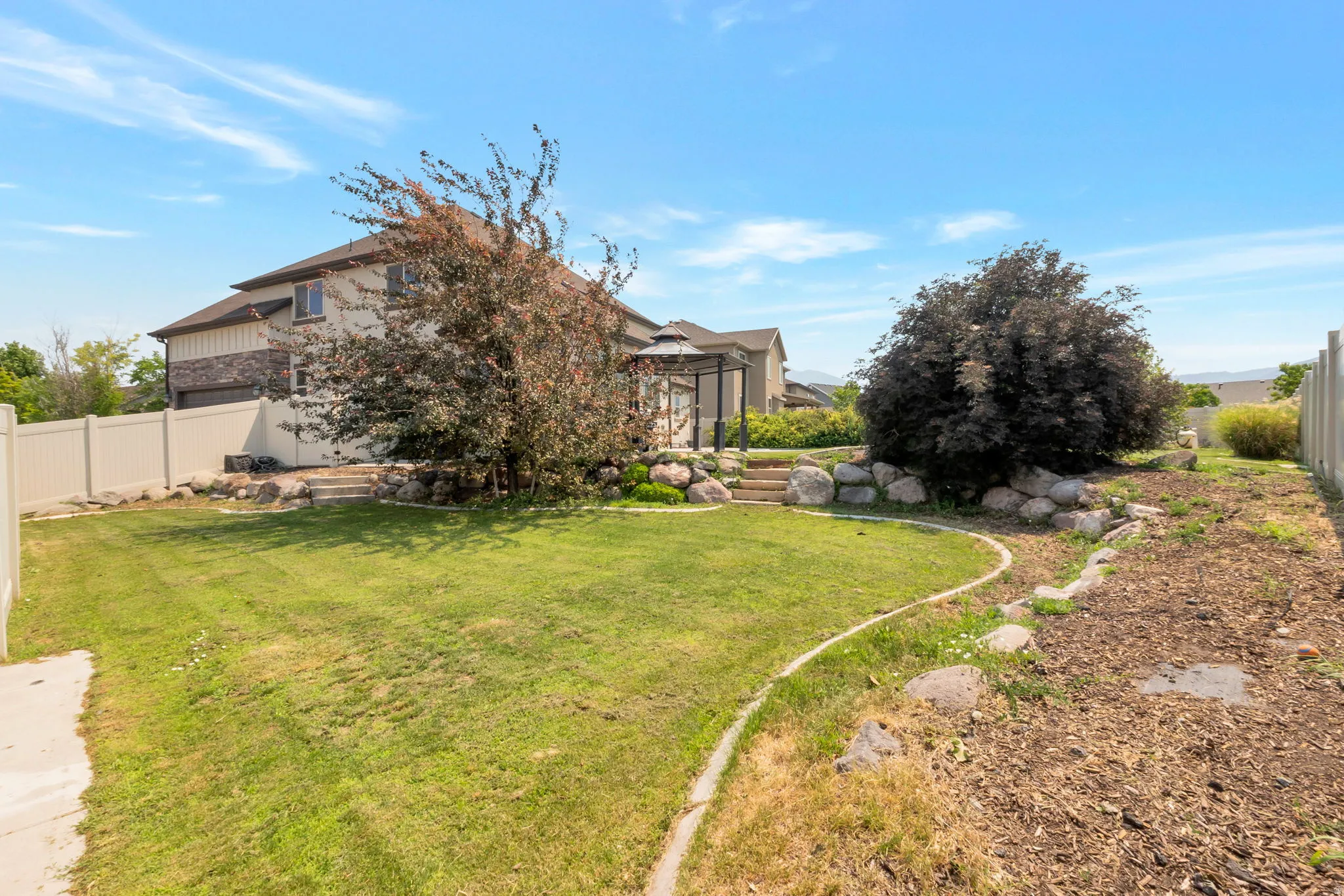 Spacious backyard featuring a manicured lawn, established trees, and a gazebo structure