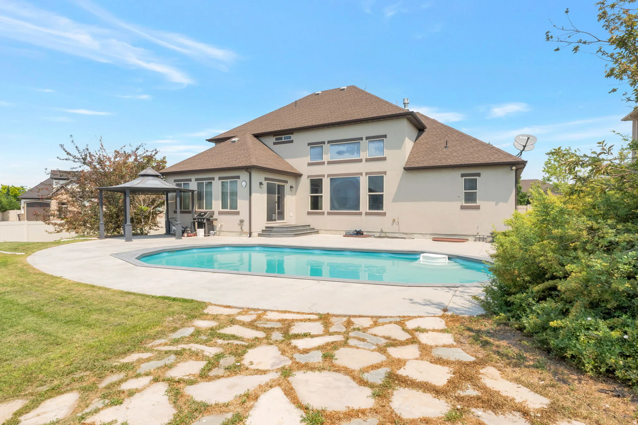 Expansive backyard featuring a large in-ground swimming pool with a surrounding concrete patio, a decorative stone pathway, a gazebo, and stucco exterior