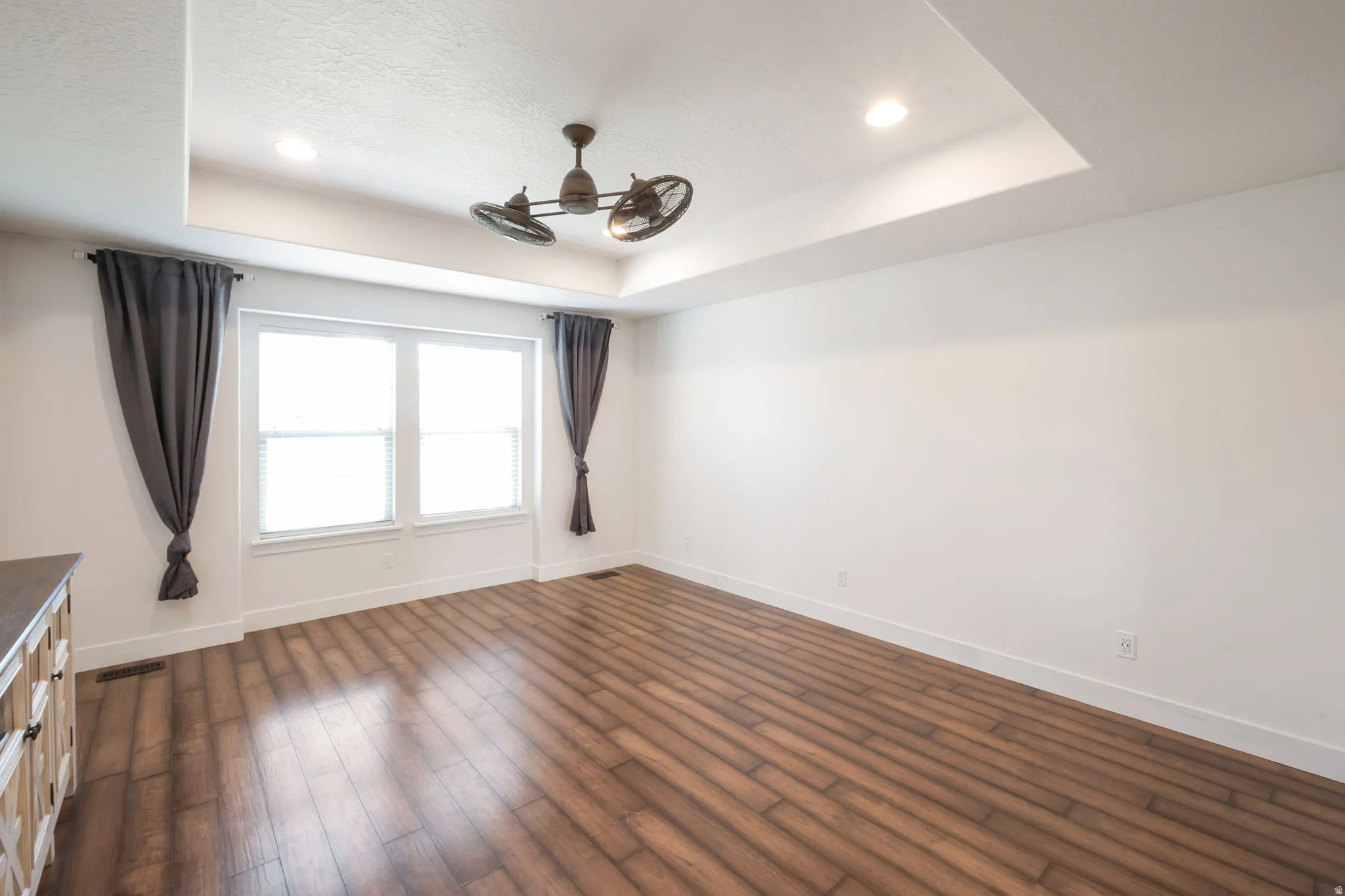Spacious room featuring wood-finish flooring, a tray ceiling with recessed lighting, and a multi-blade ceiling fan