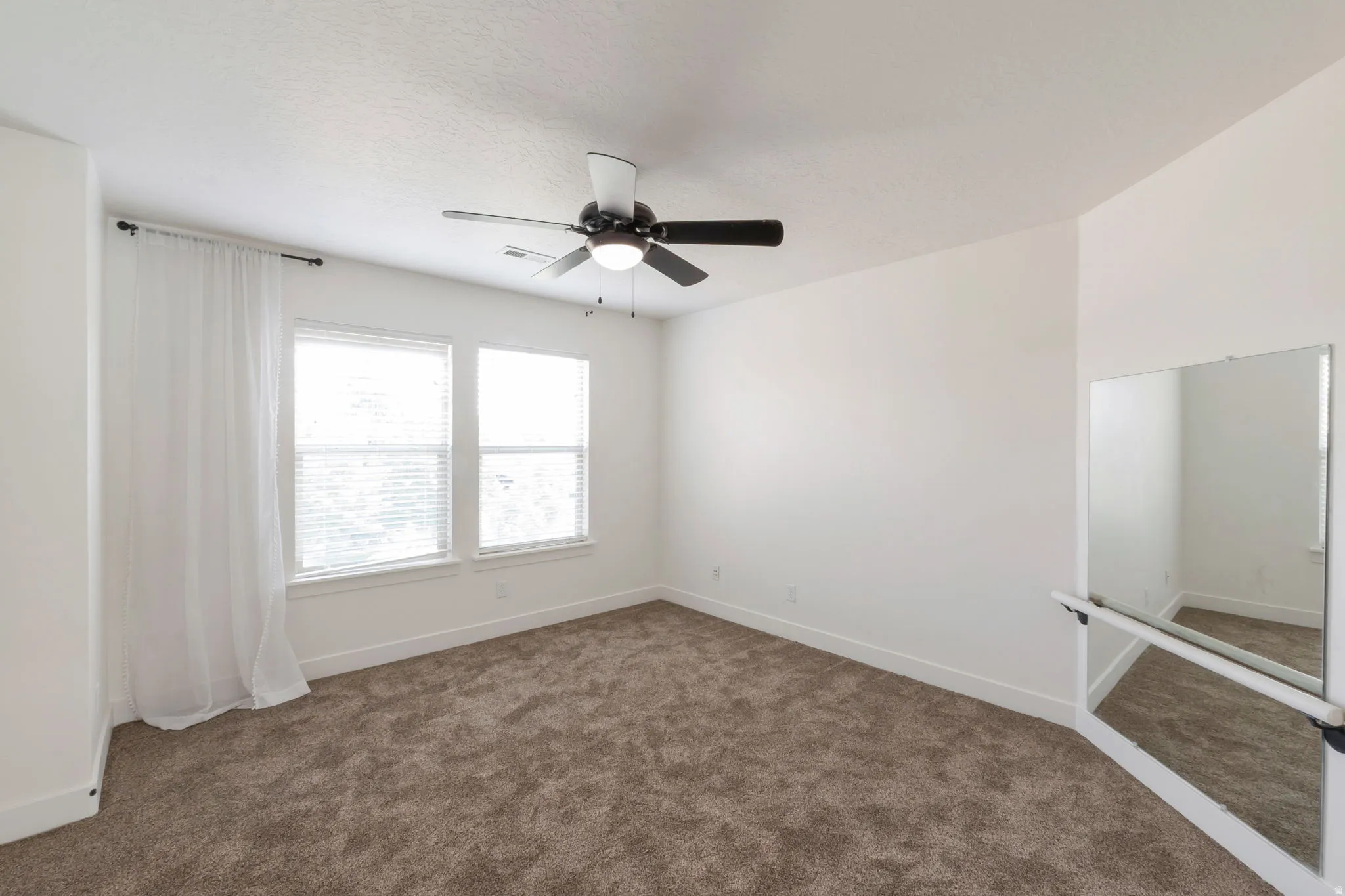 Carpeted room with a ceiling fan light fixture, two windows with blinds, and a mirrored wall with a ballet barre