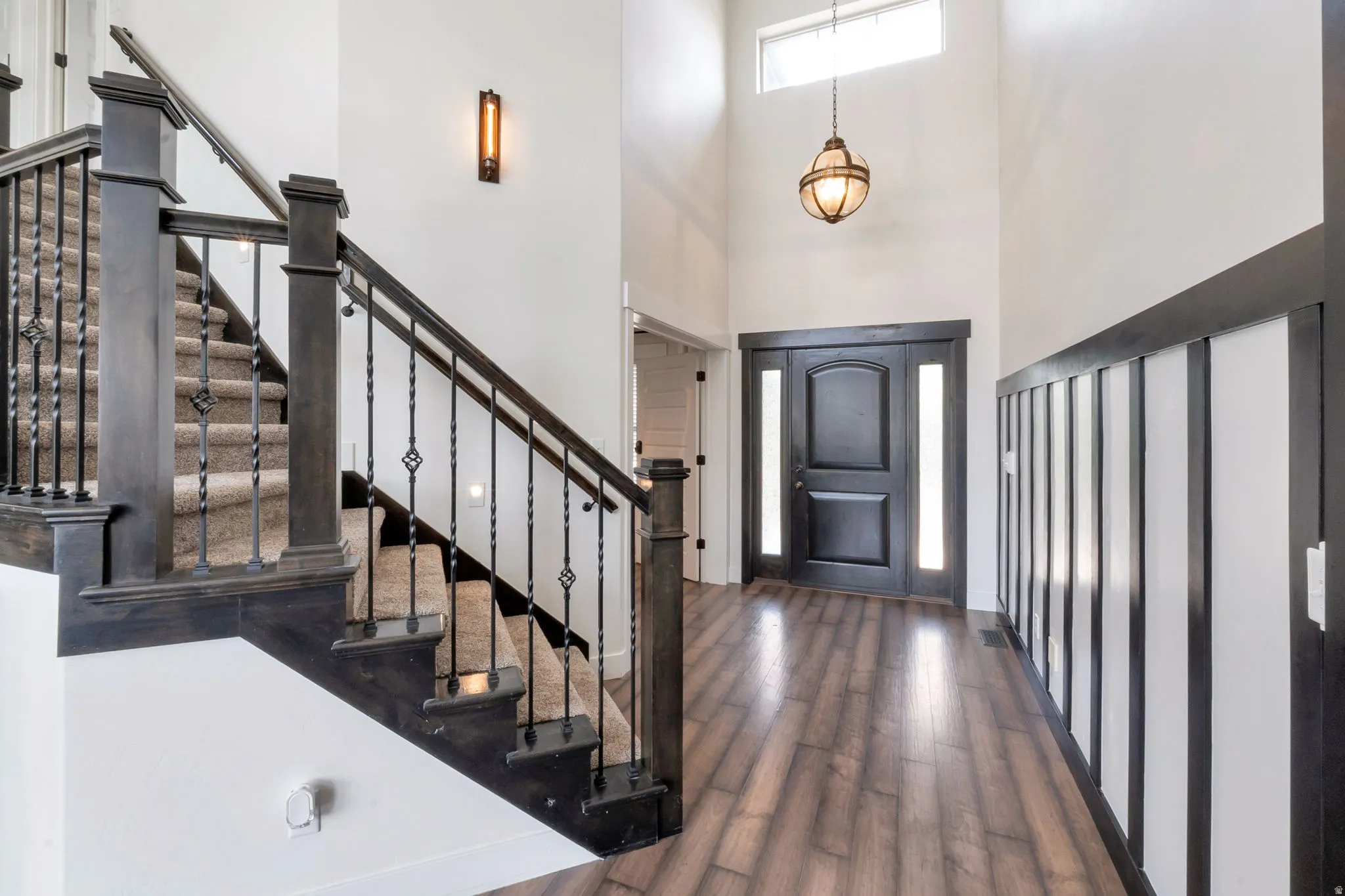 Entry foyer featuring wood-finish flooring and a carpeted staircase with dark wood newel posts and wrought iron balusters