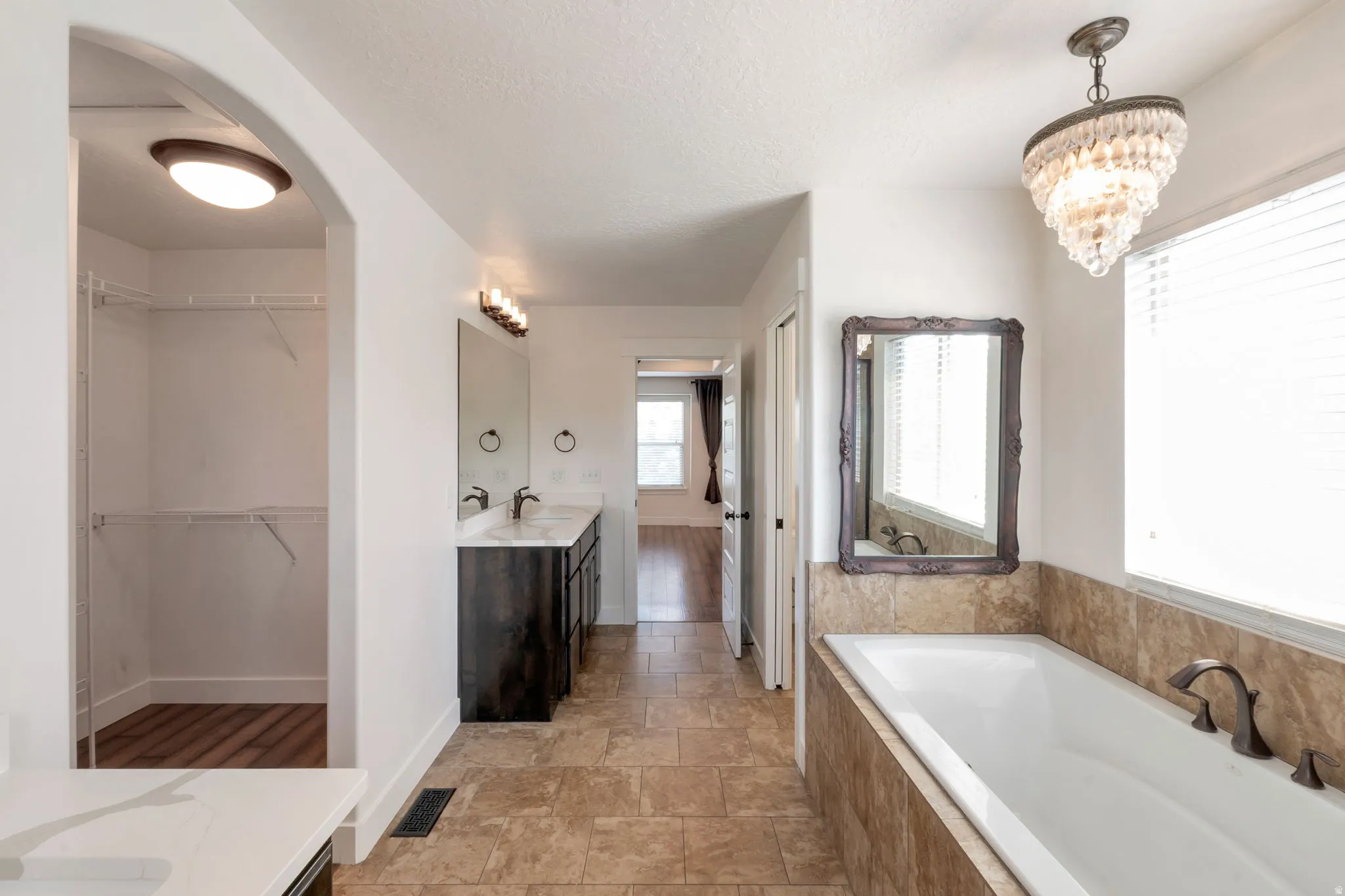 Bathroom featuring a soaking tub with tile surround, a dual vanity with a dark wood-finish cabinet and stone countertop, and a separate walk-in closet with wire shelving