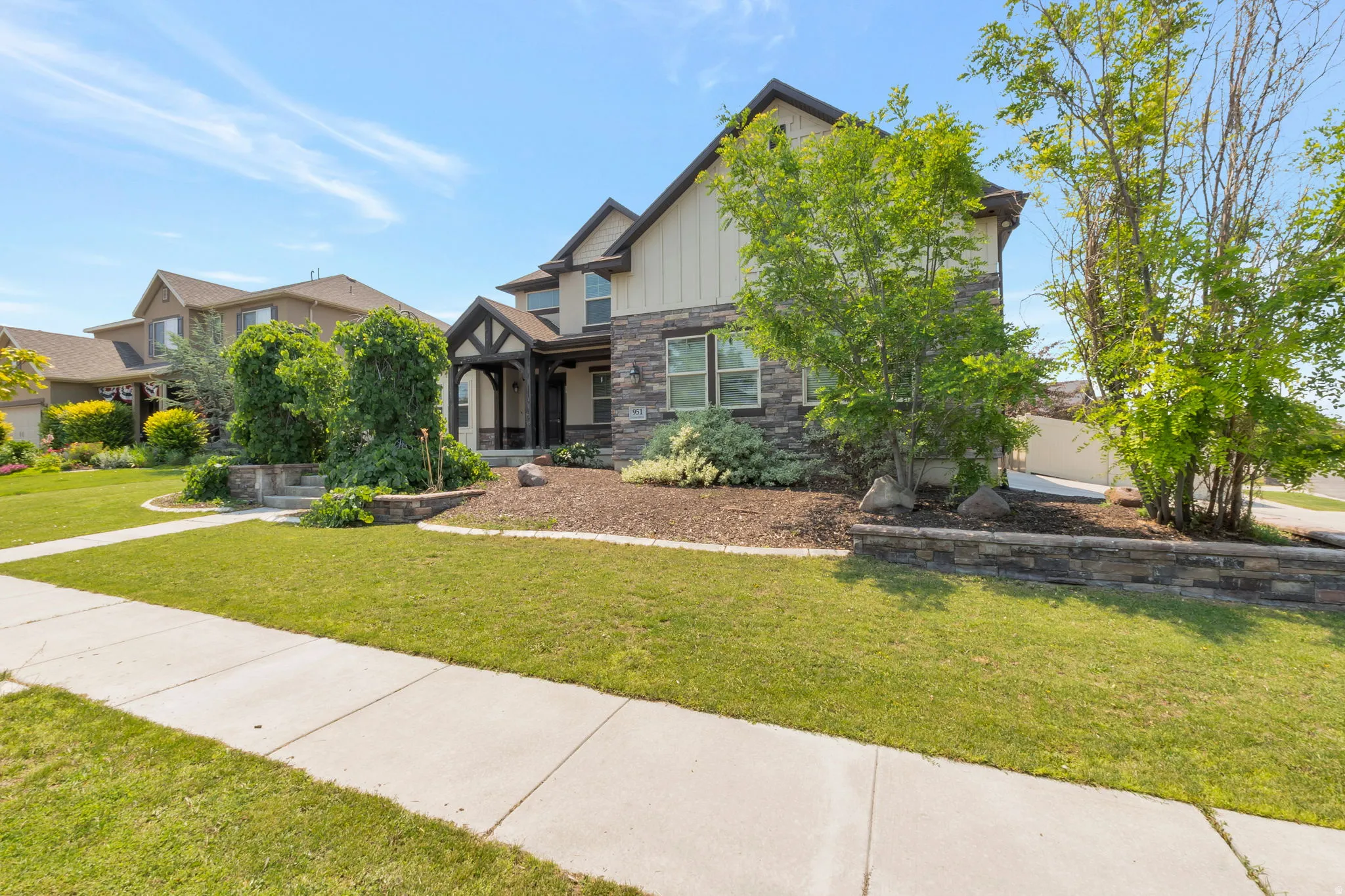 Two-story residence featuring a stone and siding exterior, a covered entryway with dark wood accents, and a landscaped front yard with a stone retaining wall