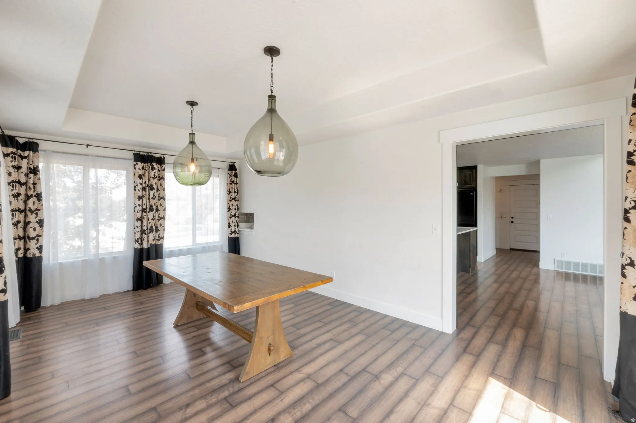 Spacious room featuring wood-finish flooring, a tray ceiling, and dual pendant lighting fixtures