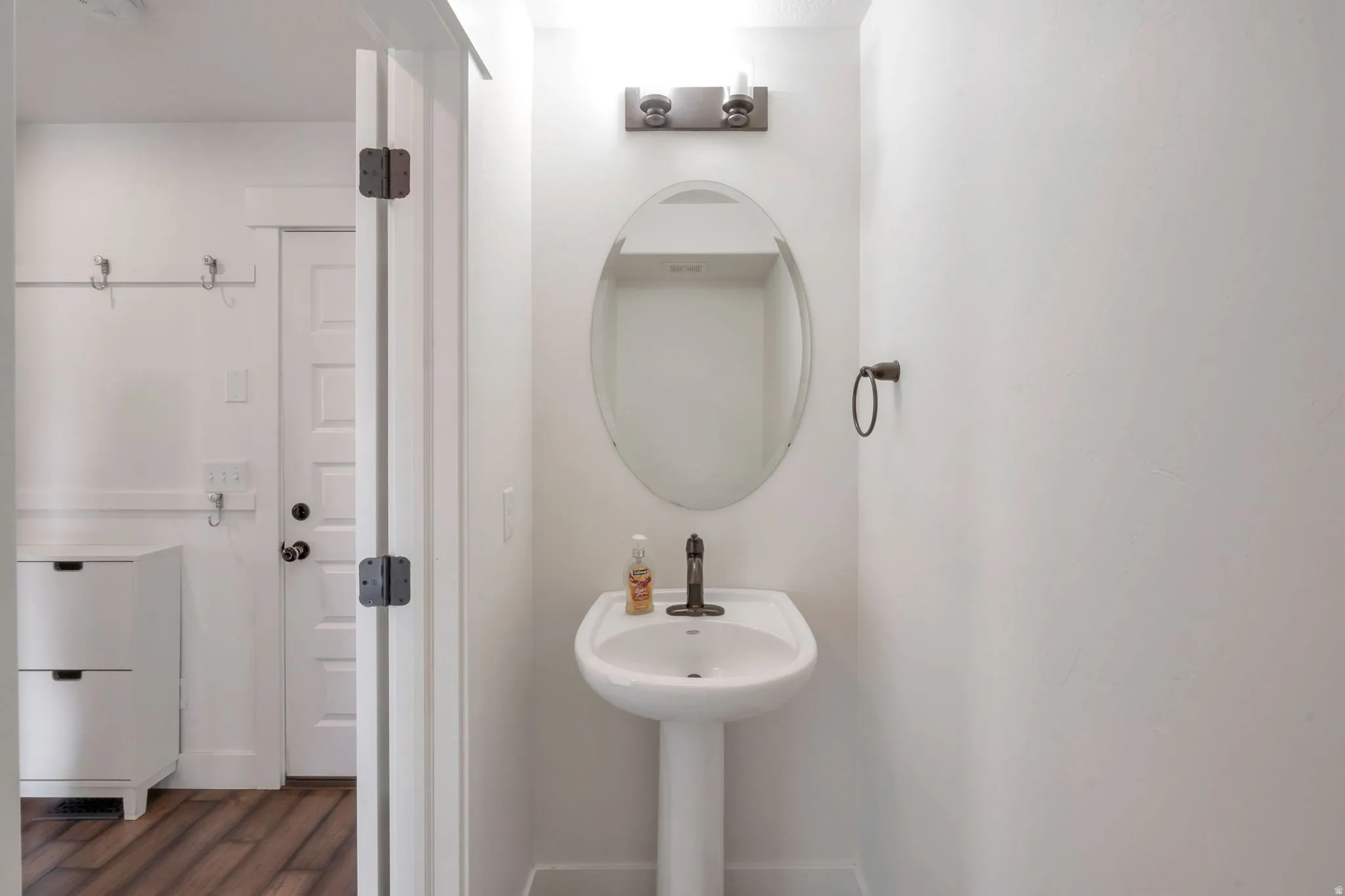 Pedestal sink with dark bronze faucet, oval mirror, and wall-mounted light fixture