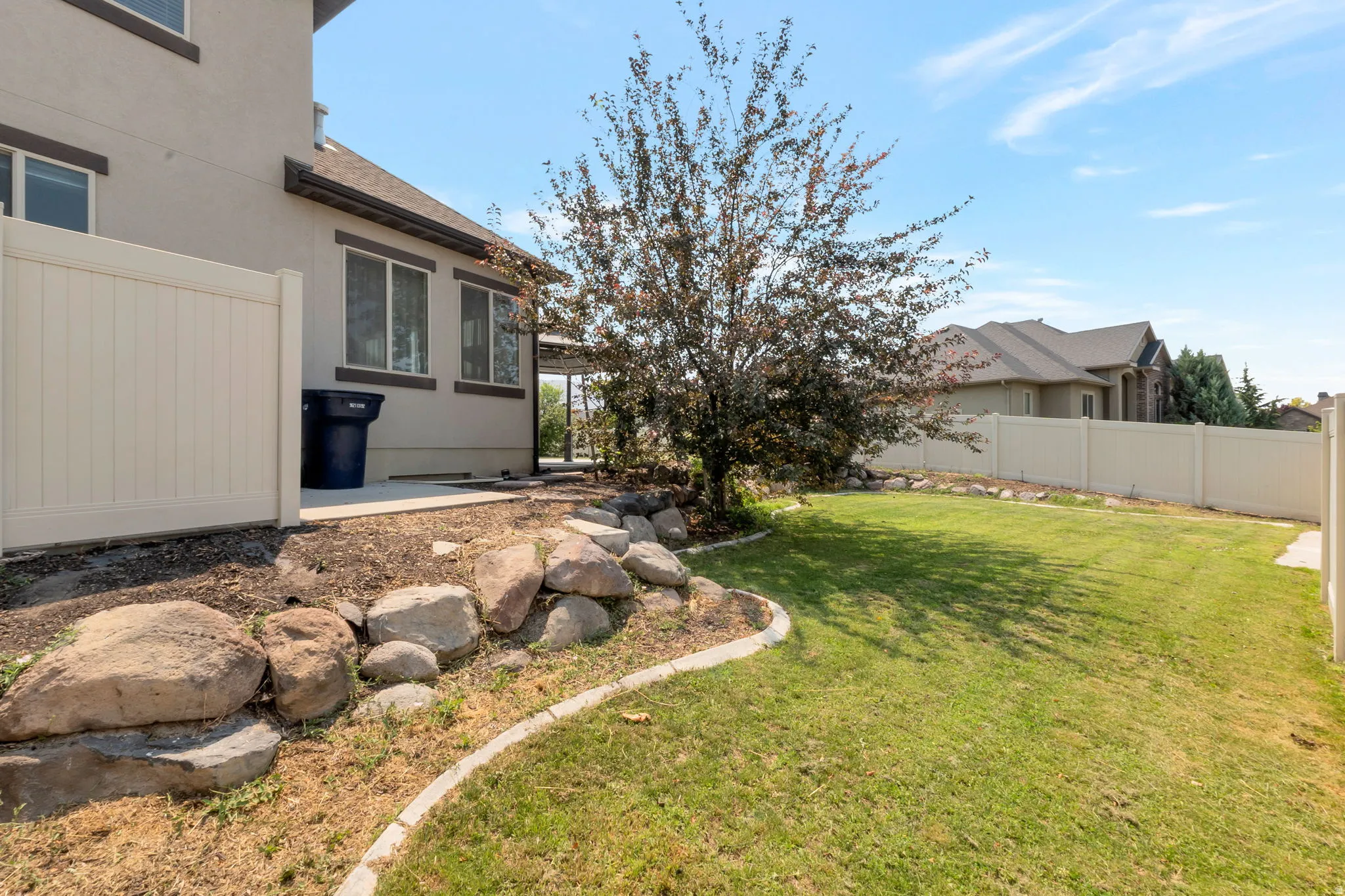 Spacious backyard featuring a manicured lawn, established tree, and decorative rock landscaping