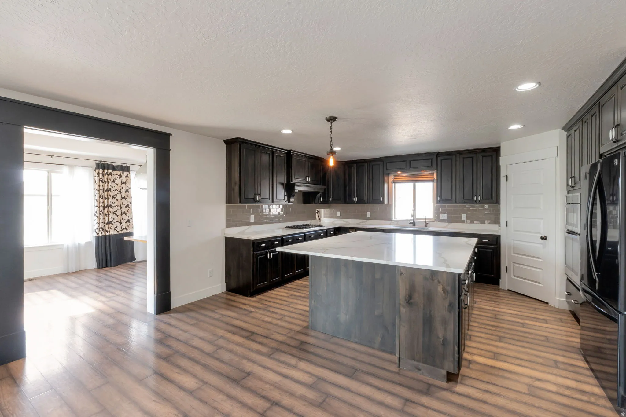 Kitchen featuring wood-finish flooring, dark cabinetry, recessed lighting, and a kitchen island with a light-toned countertop