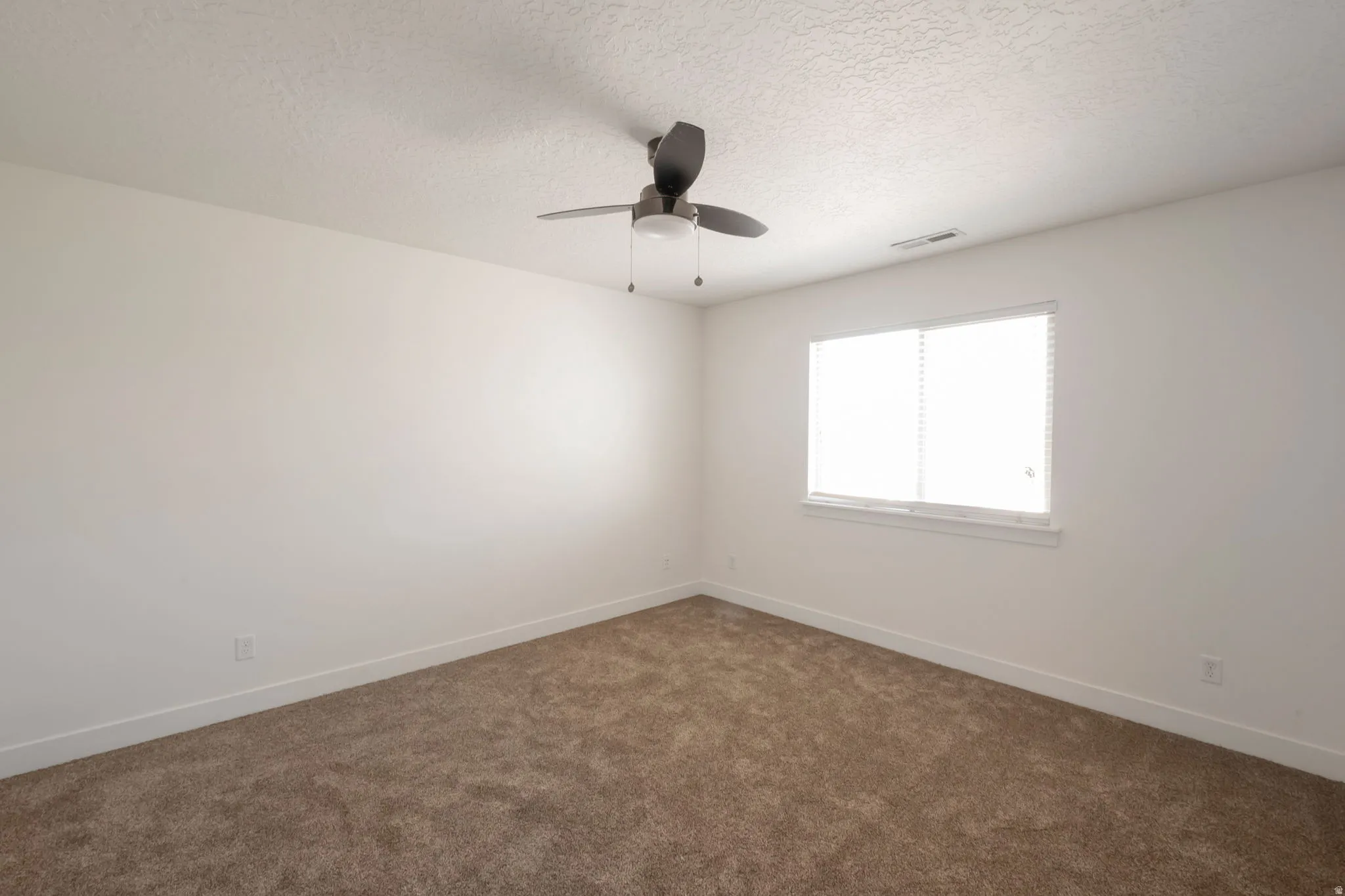 Carpeted room featuring a ceiling fan, a window with blinds, and white baseboards