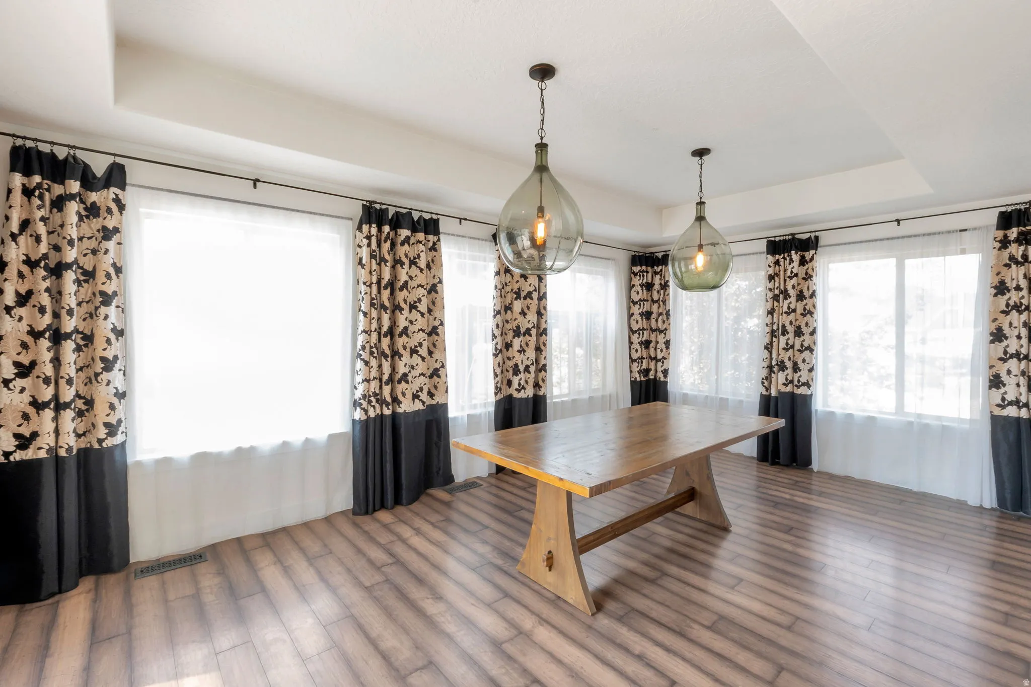 Spacious room featuring wood-finish flooring and multiple windows with sheer and patterned curtains