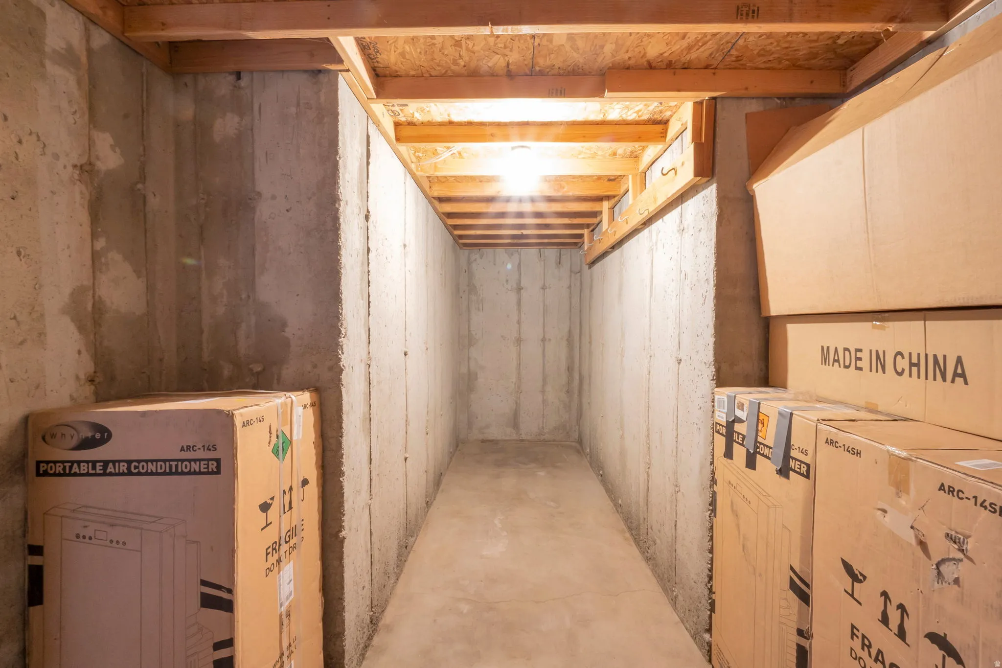 Concrete basement hallway featuring exposed wood ceiling joists and a concrete floor