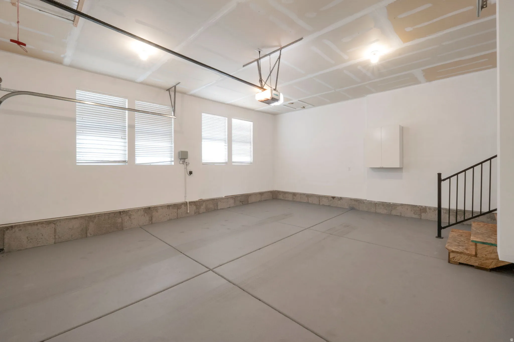 Spacious garage with a concrete floor, multiple windows for natural light, built-in storage cabinet, and a staircase with a black metal railing