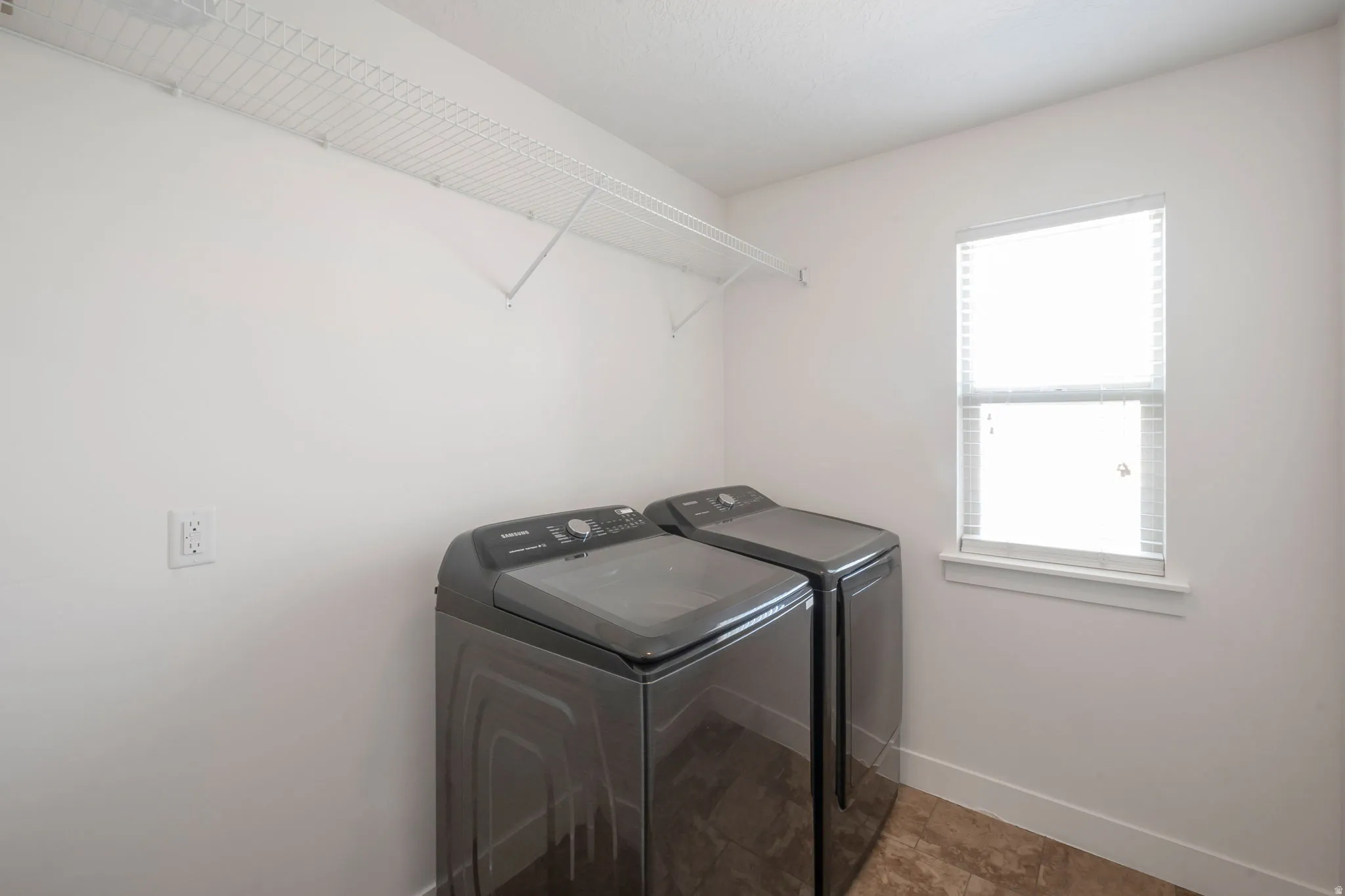 Dedicated laundry area featuring wire shelving, a window with blinds, and tile flooring
