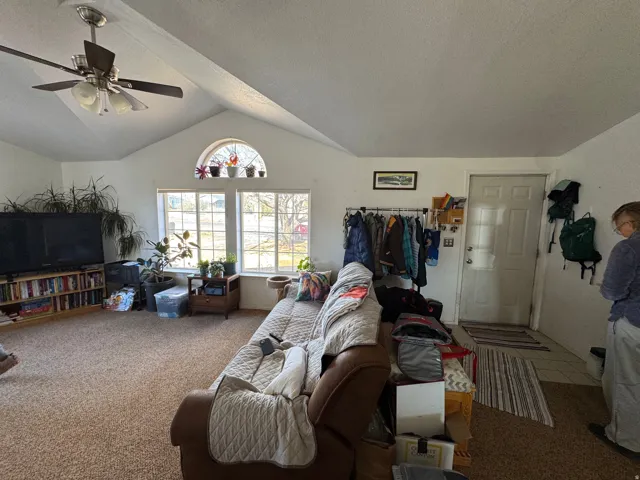 Living area featuring vaulted ceilings, a ceiling fan, and large windows with an arched transom