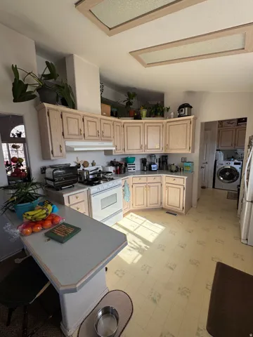 Kitchen featuring light wood cabinetry, white appliances, a peninsula with a light-toned countertop, and recessed ceiling lighting