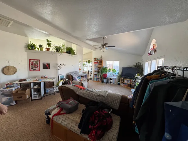 Spacious living area featuring a vaulted ceiling with a ceiling fan, multiple windows for natural light, and an arched transom window