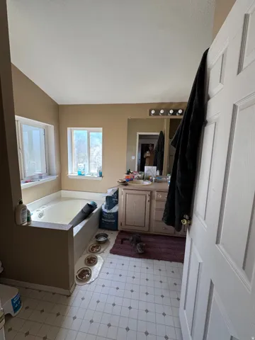 Bathroom featuring a built-in soaking tub with a surrounding ledge, a vanity with a light wood-finish cabinet and countertop, and a mirror with a four-light fixture