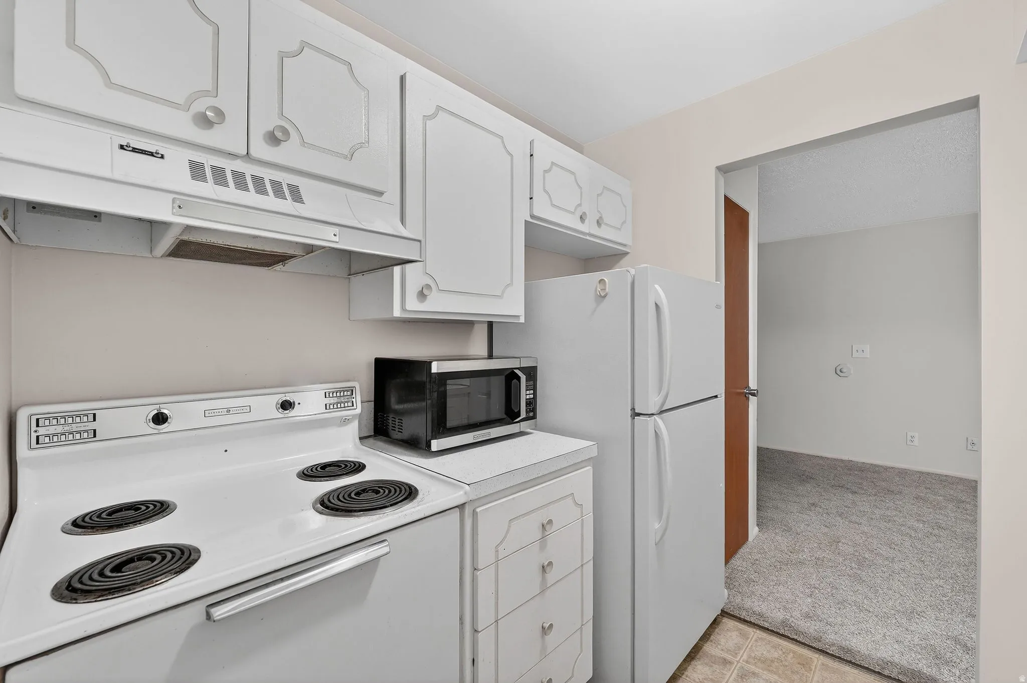 Kitchen featuring white appliances, light carpet, white cabinetry, and light countertops