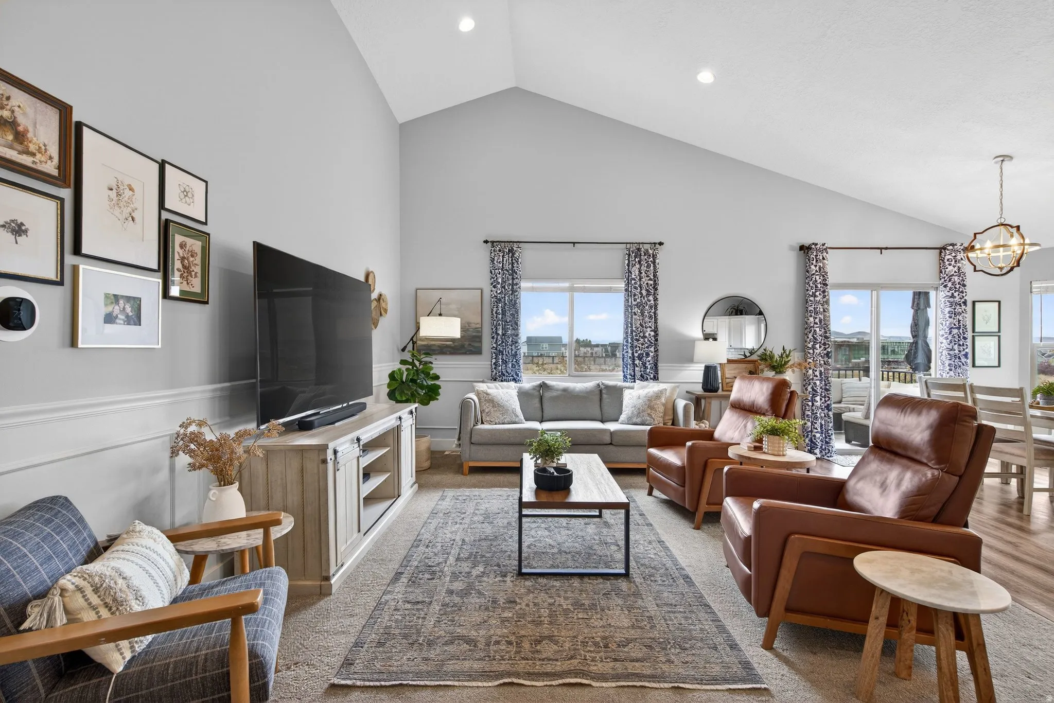 Carpeted living area featuring a wainscoted wall, a chandelier, vaulted ceiling, a decorative wall, and healthy amount of natural light
