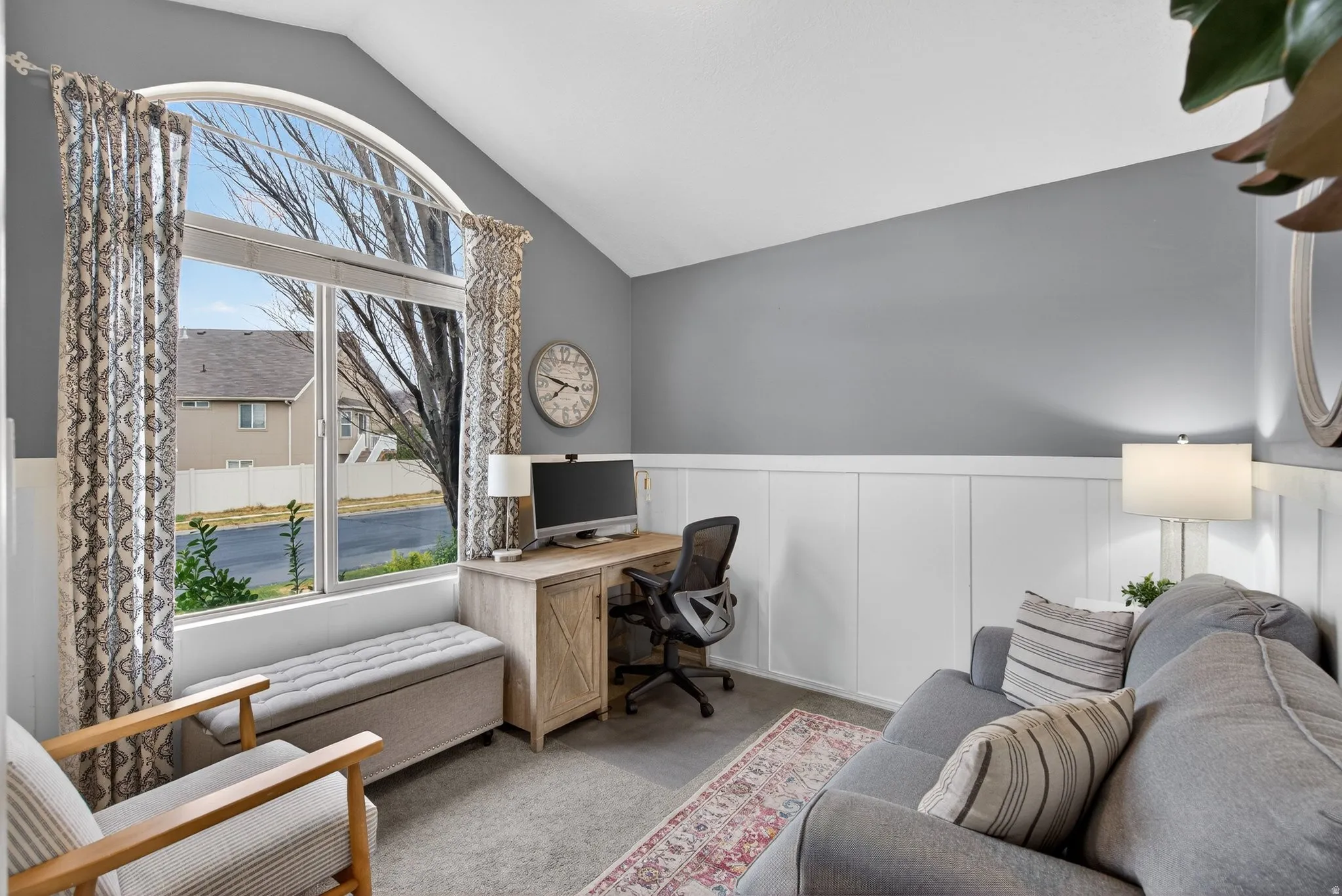 Carpeted home office featuring wainscoting, lofted ceiling, healthy amount of natural light, and a decorative wall