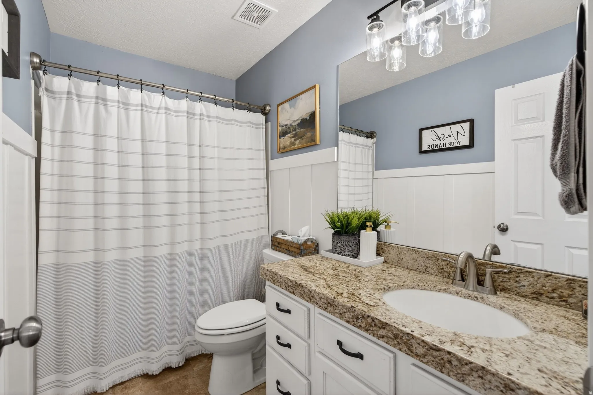 Bathroom featuring vanity, a shower with shower curtain, a wainscoted wall, a decorative wall, and a textured ceiling
