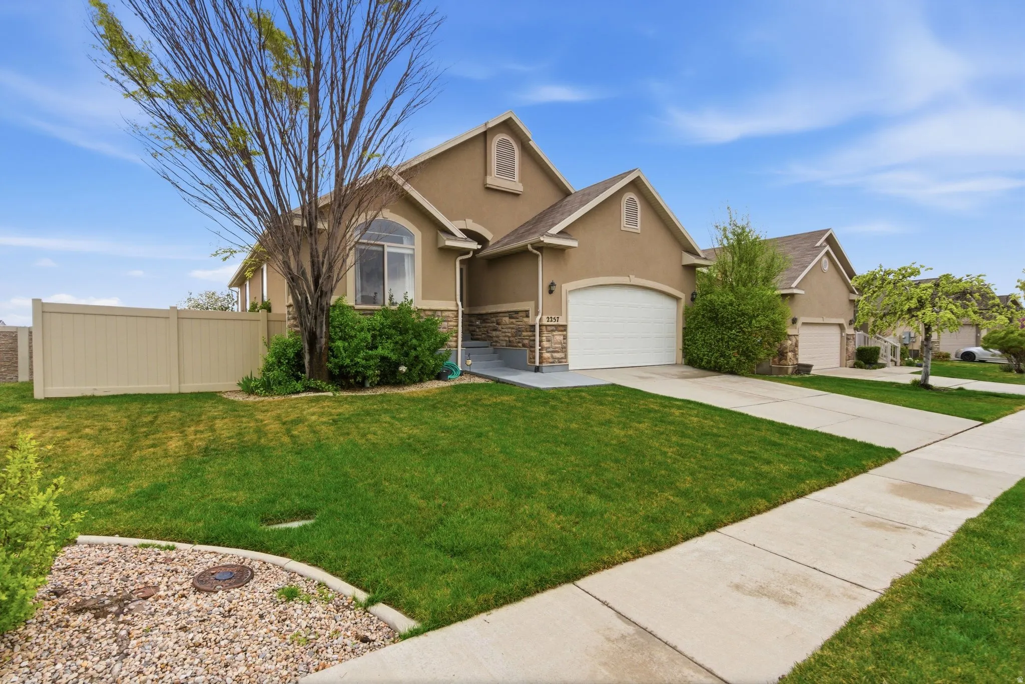 View of front of property with stucco siding, driveway, stone siding, and a garage