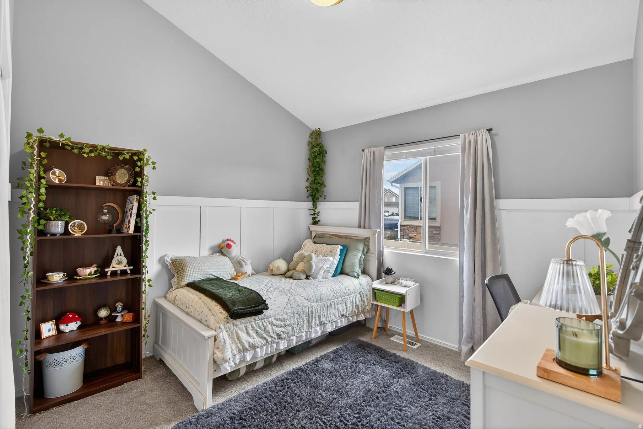 Bedroom with carpet floors, vaulted ceiling, wainscoting, and a decorative wall
