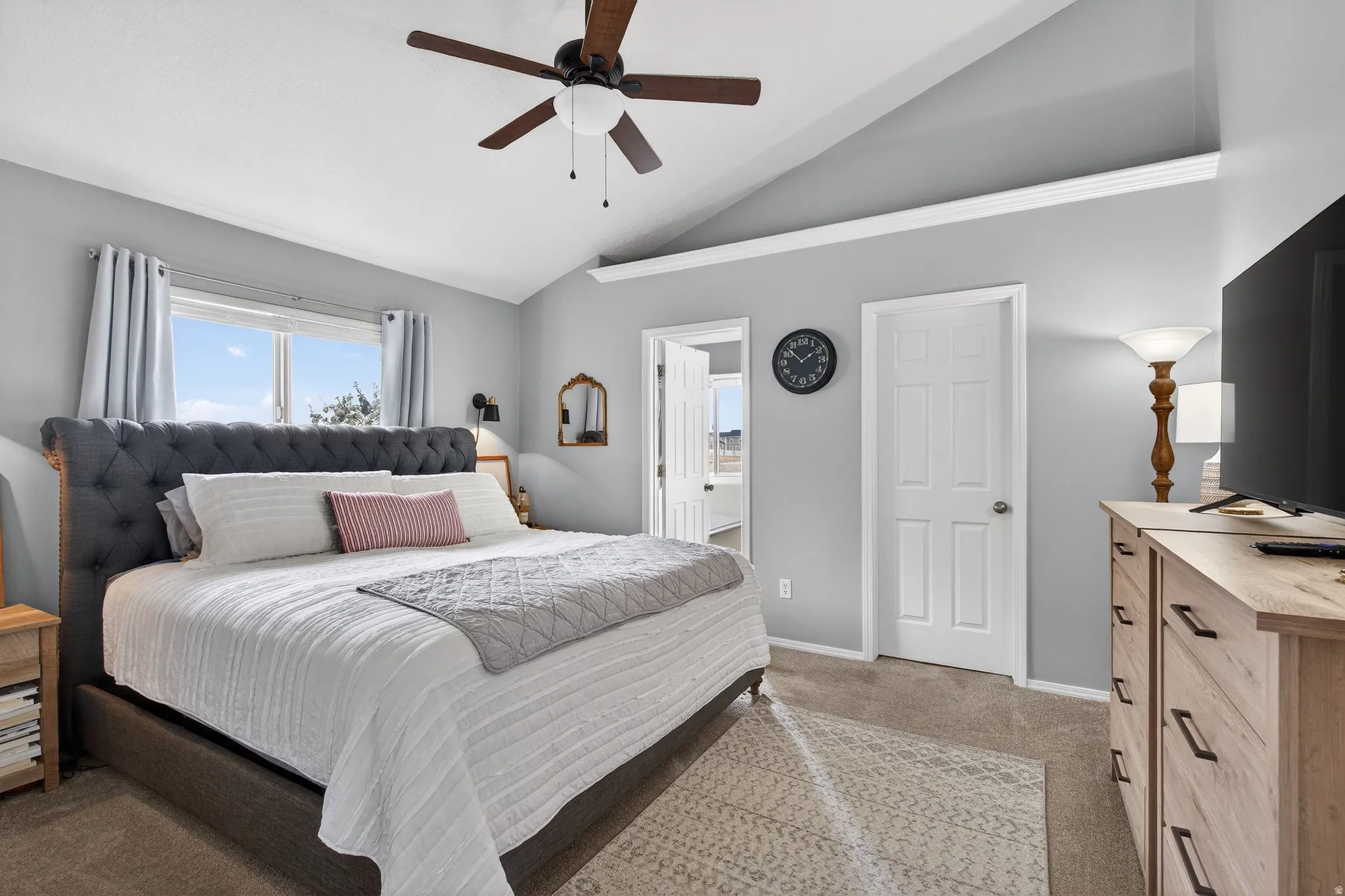 Bedroom with light colored carpet, vaulted ceiling, ceiling fan, and connected bathroom