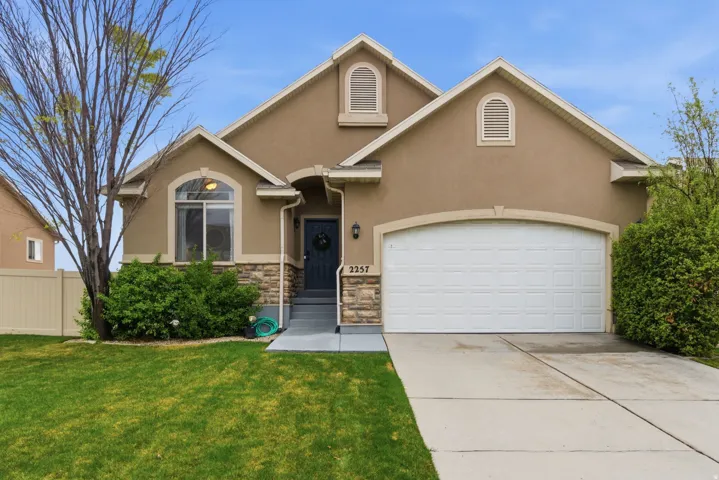 View of front of house featuring stucco siding, driveway, an attached garage, and stone siding