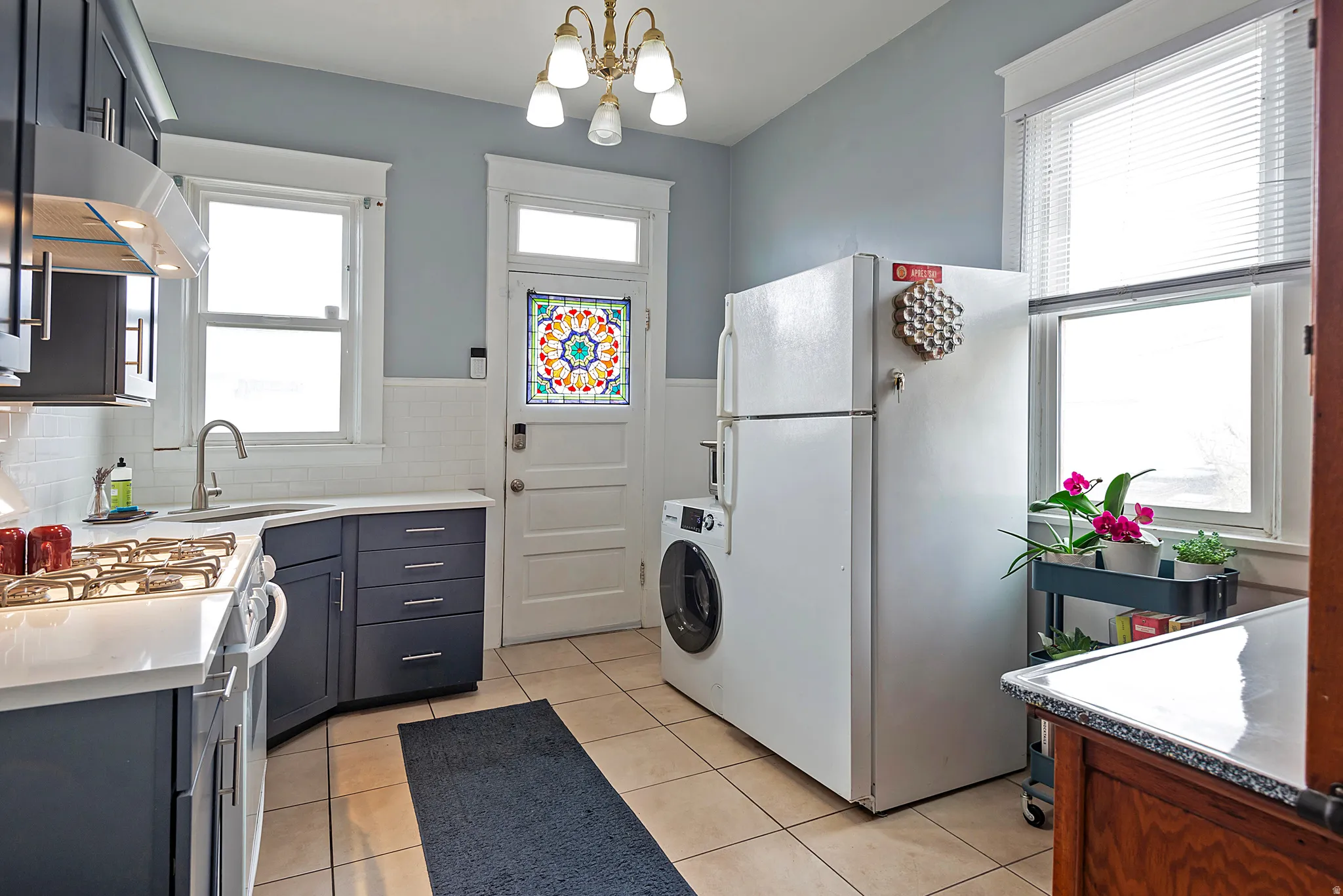 Kitchen with freestanding refrigerator, range with gas stovetop, washer / clothes dryer, suspended lighting, and light stone counters