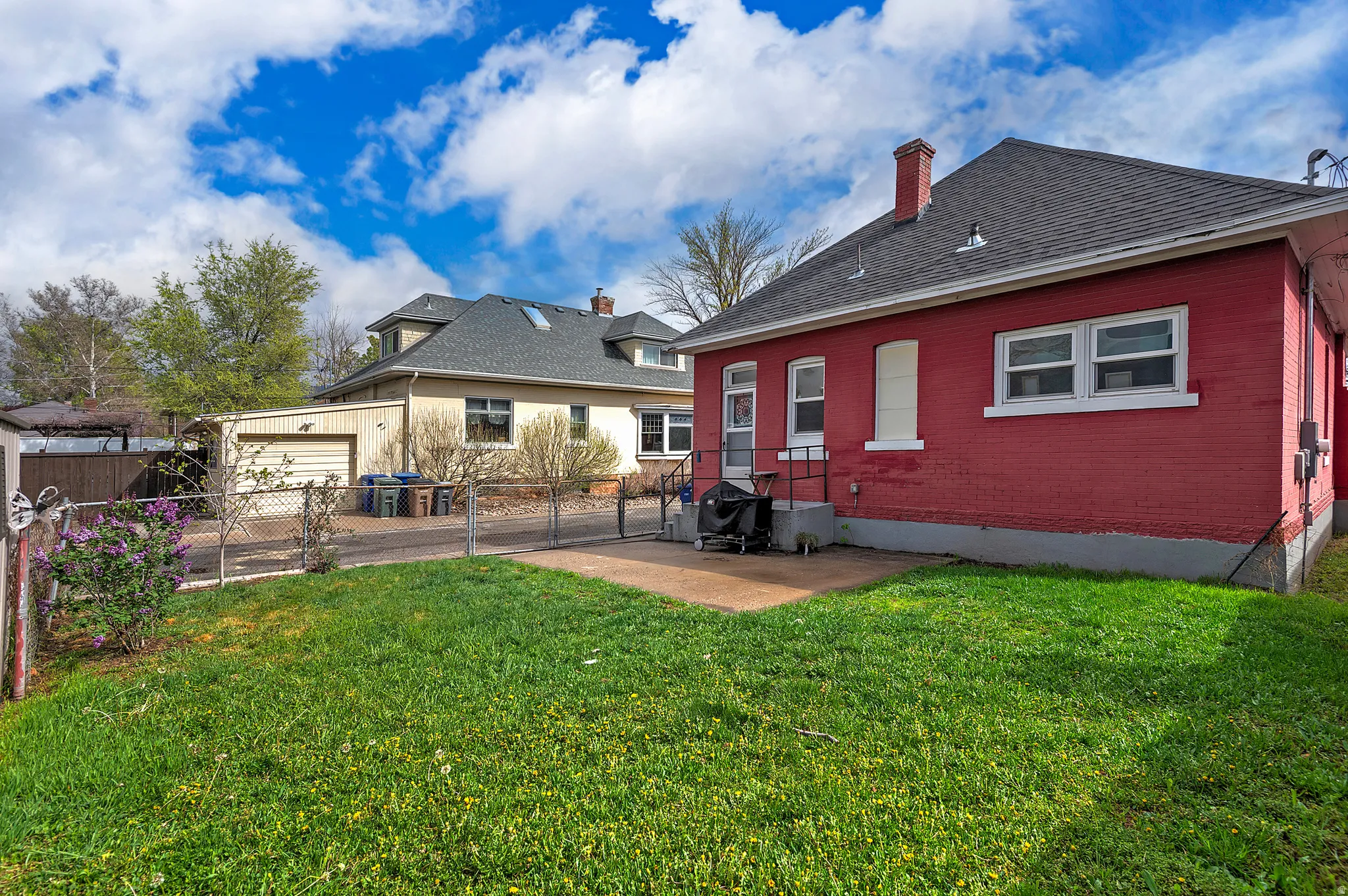 Rear view of property featuring a gate, brick siding, a chimney, a patio area, and a shingled roof