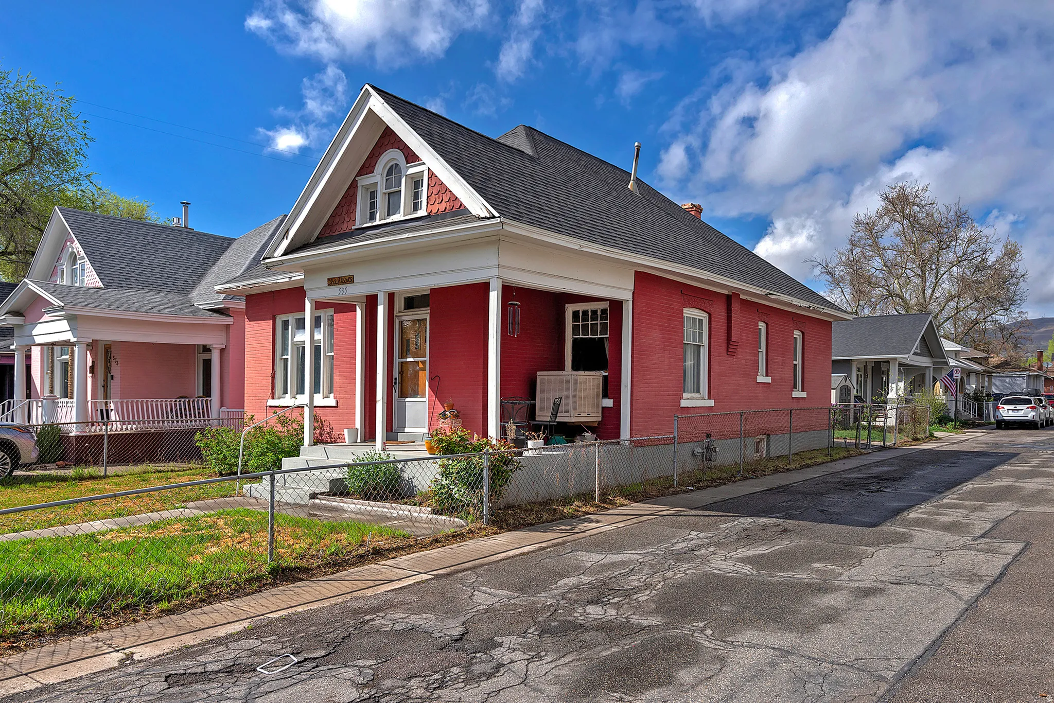 View of front of property featuring covered porch, brick siding, roof with shingles, a chimney, and a fenced front yard