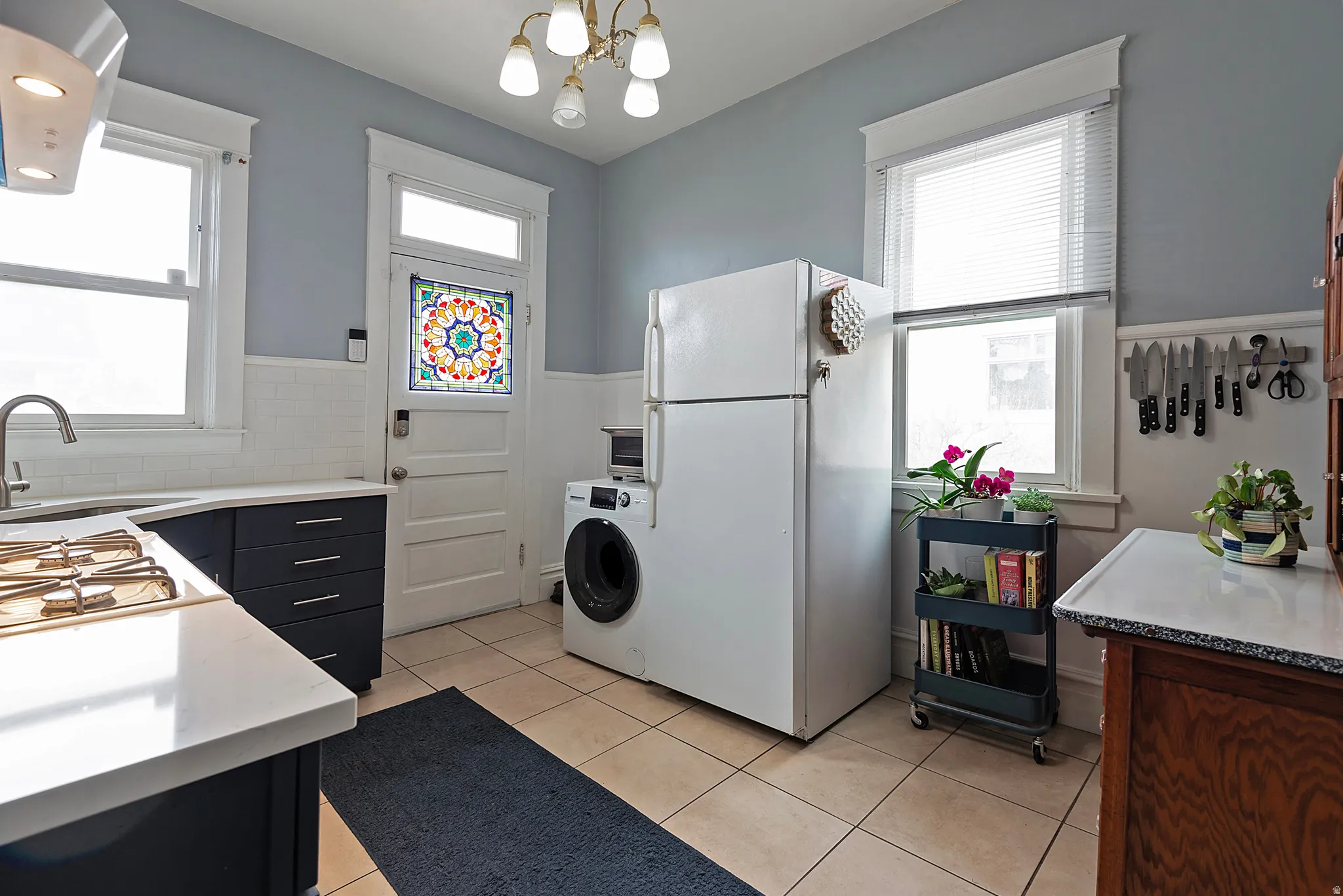 Kitchen with white appliances, island exhaust hood, washer / dryer, light tile patterned floors, and hanging lights