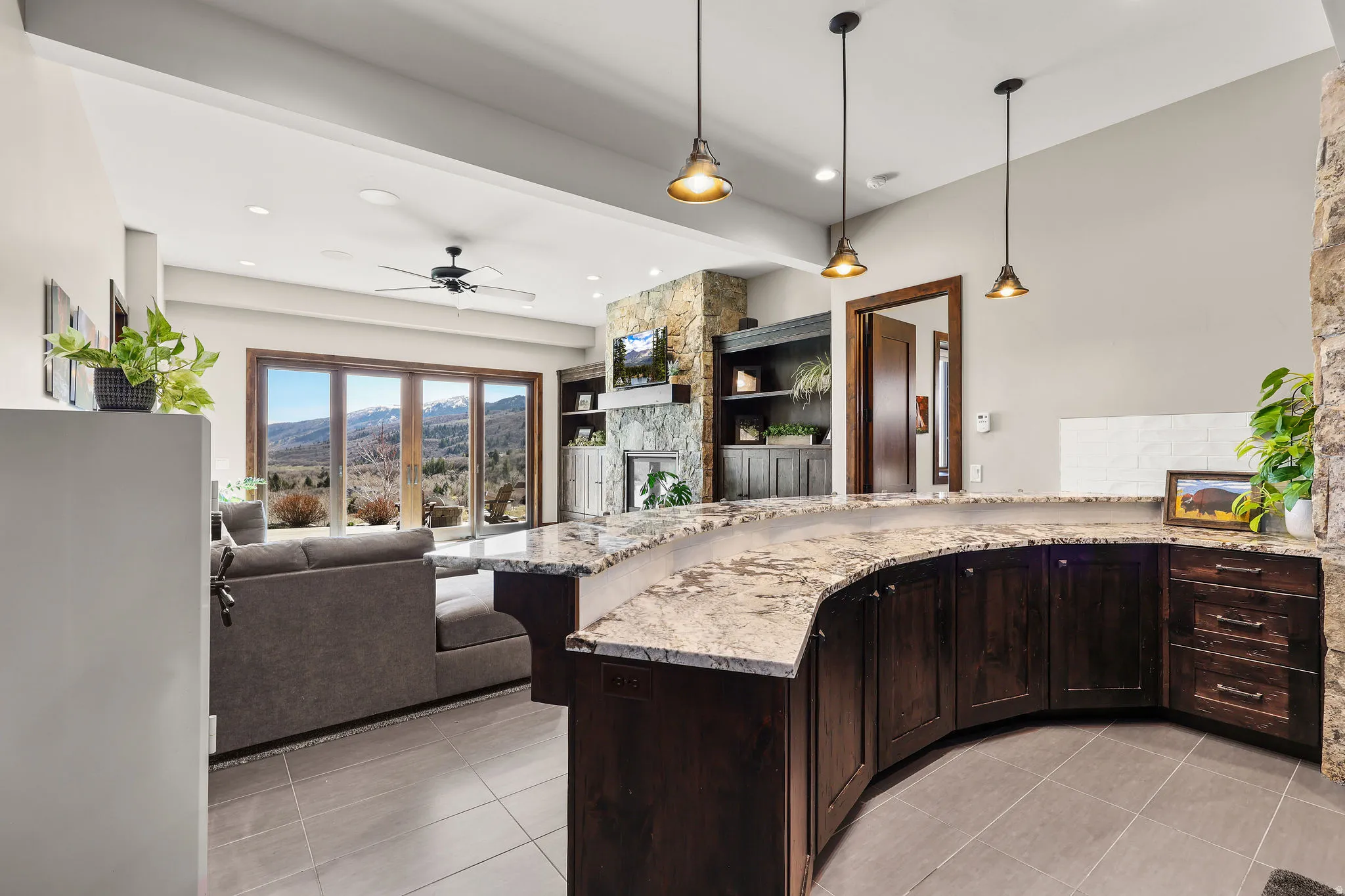 Kitchen with dark wood finish cabinetry, a peninsula, hanging light fixtures, a ceiling fan, and open floor plan