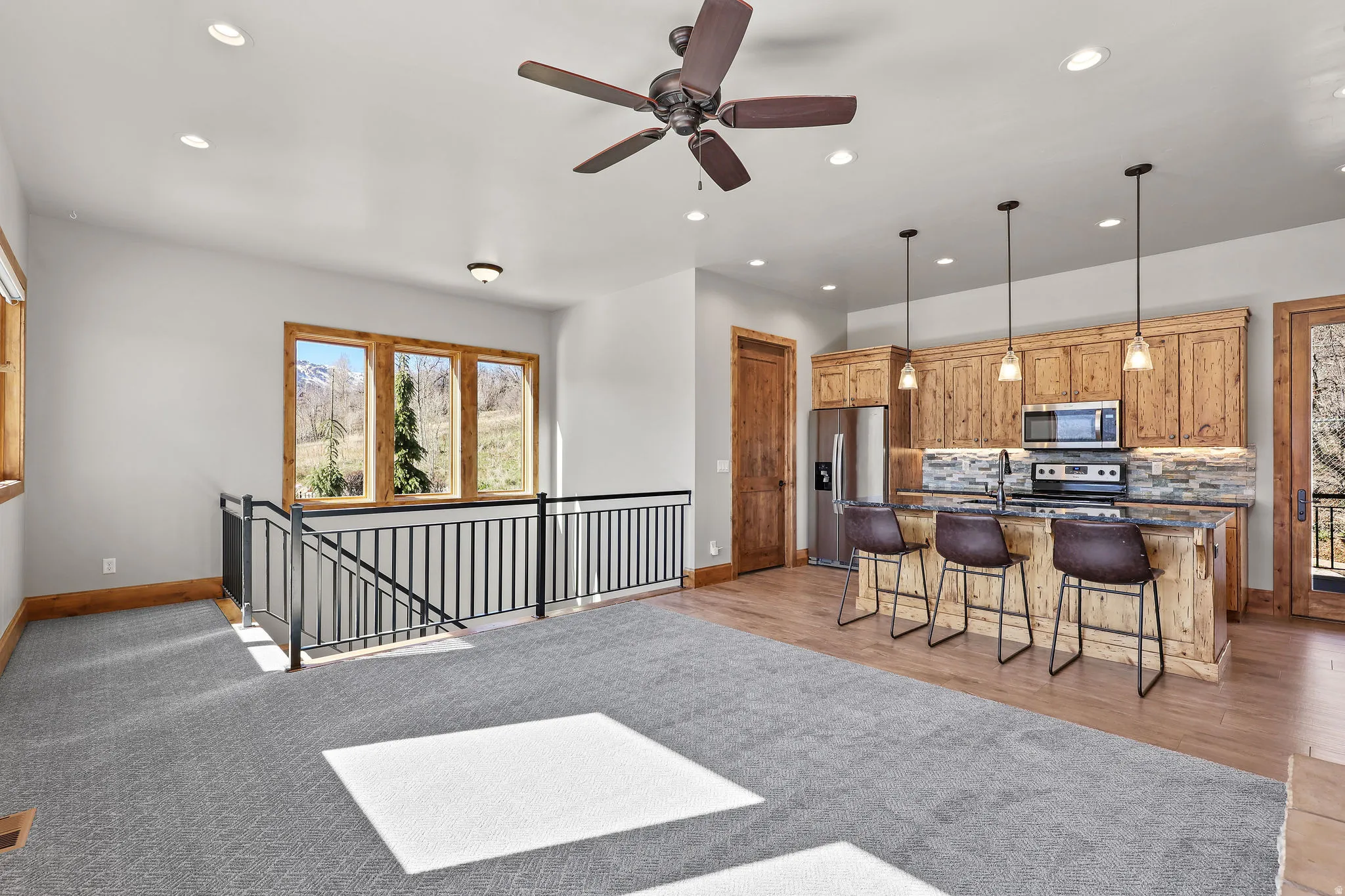Kitchen with ceiling fan, stainless steel appliances, a kitchen island with sink, backsplash, and a breakfast bar