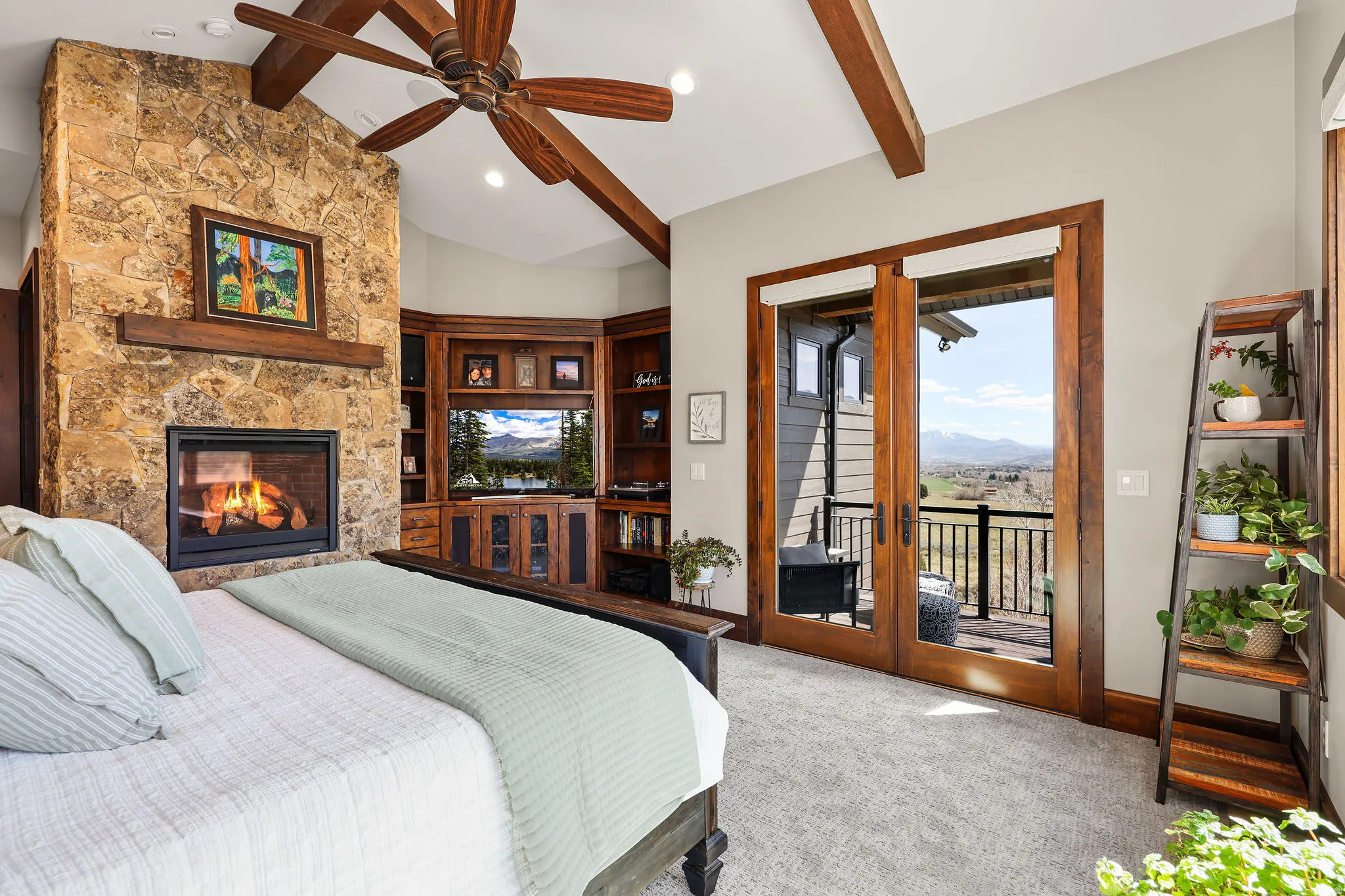 Carpeted bedroom featuring access to outside, french doors, a stone fireplace, vaulted ceiling with beams, and ceiling fan