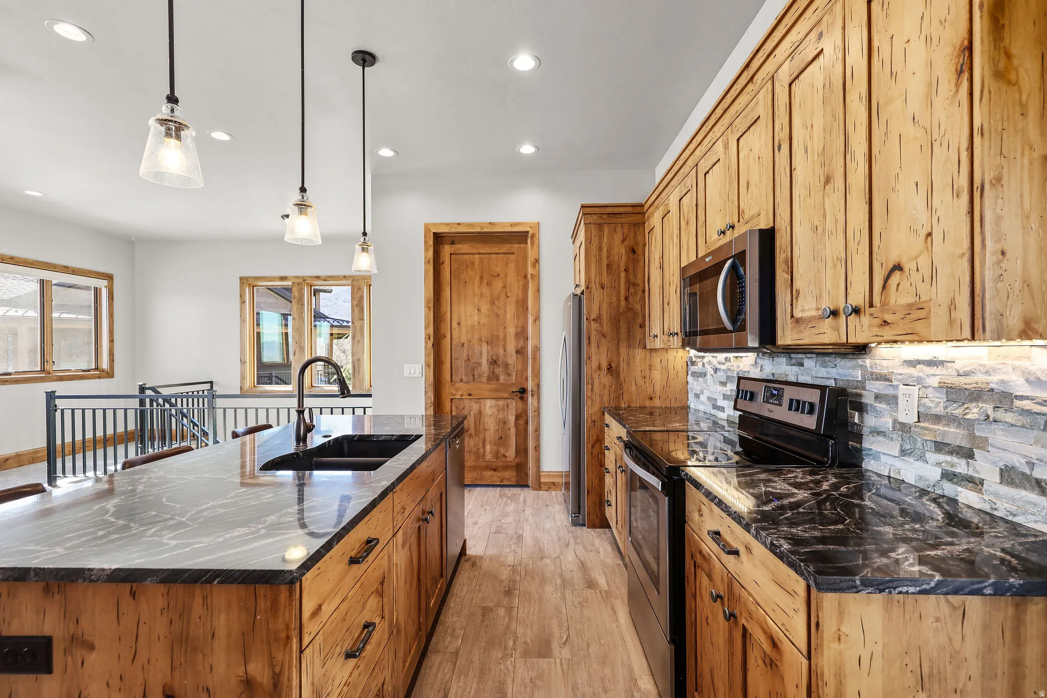 Kitchen featuring stainless steel appliances, a center island with sink, light wood-type flooring, tasteful backsplash, and decorative light fixtures