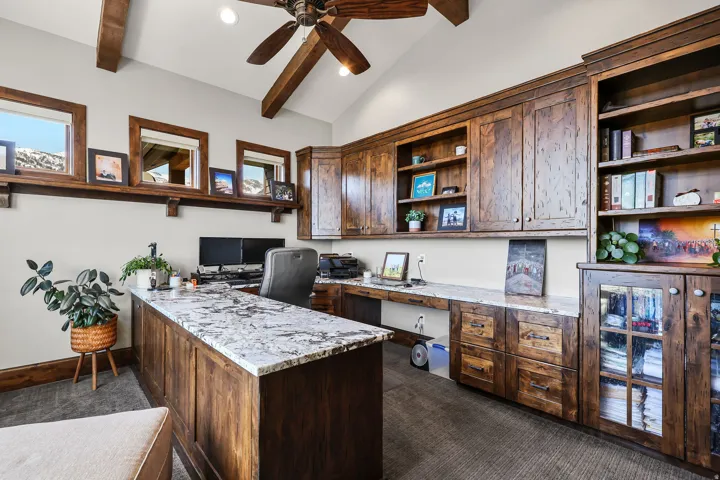 Office area with built in desk, dark colored carpet, ceiling fan, vaulted ceiling with beams, and recessed lighting