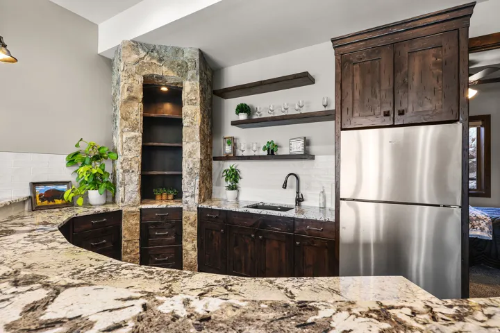 Bar area featuring freestanding refrigerator, dark wood finish cabinetry, light stone counters, open shelves, and tasteful backsplash