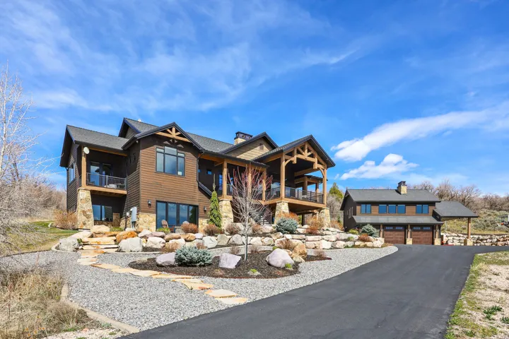 View of front of home featuring stone siding, a chimney, asphalt driveway, and a balcony