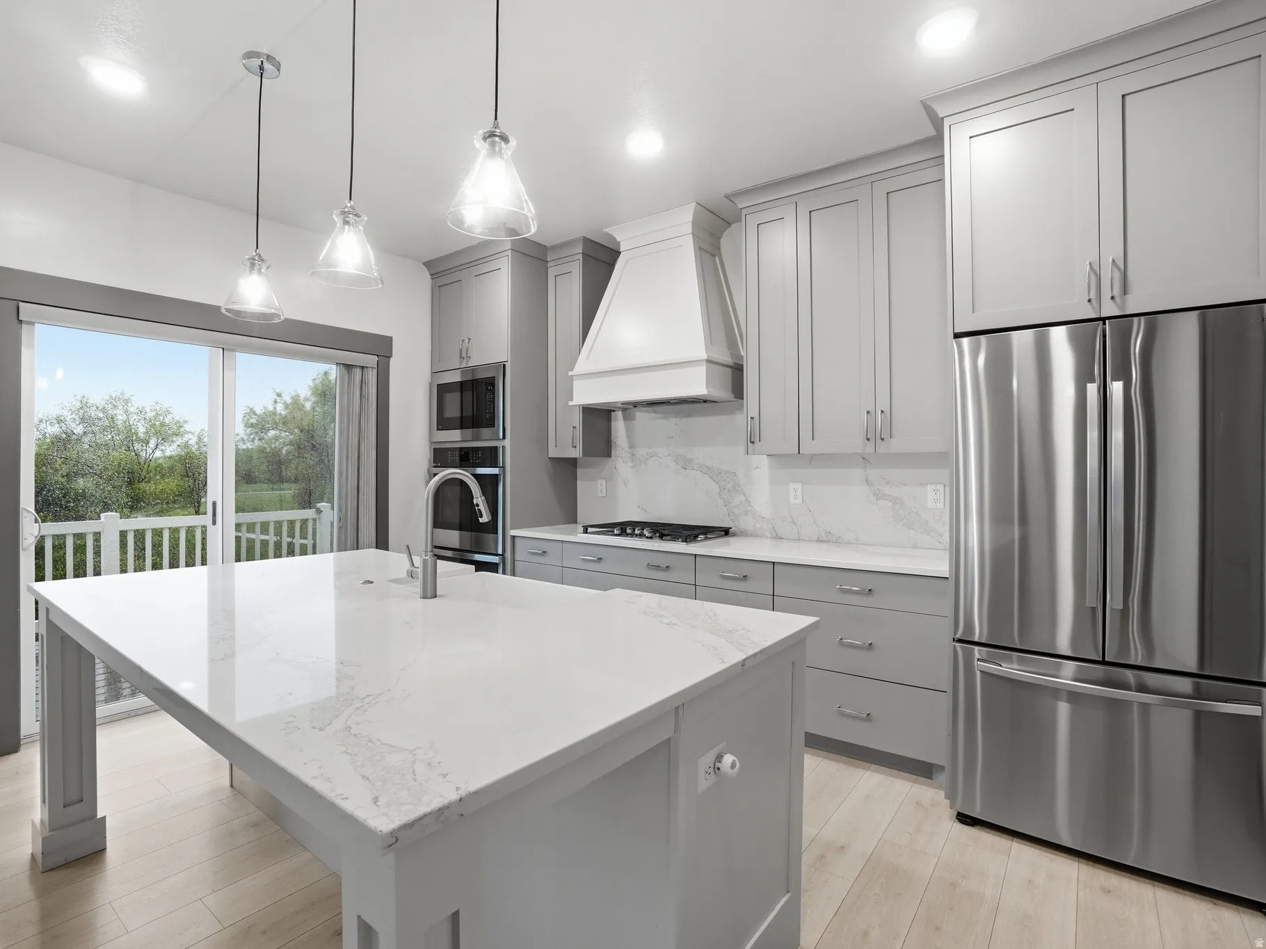 Kitchen with stainless steel appliances, light stone countertops, light wood-style flooring, decorative backsplash, and gray cabinets