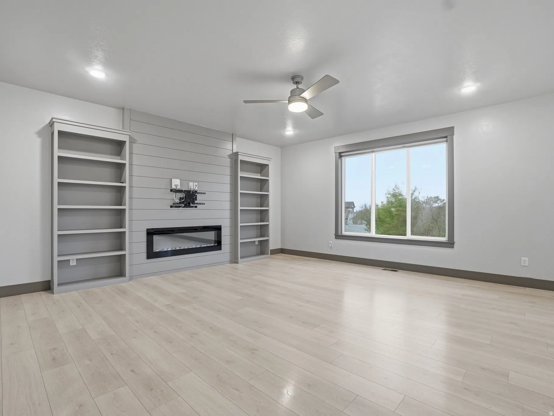 Unfurnished living room featuring ceiling fan, a fireplace, and light wood-style flooring