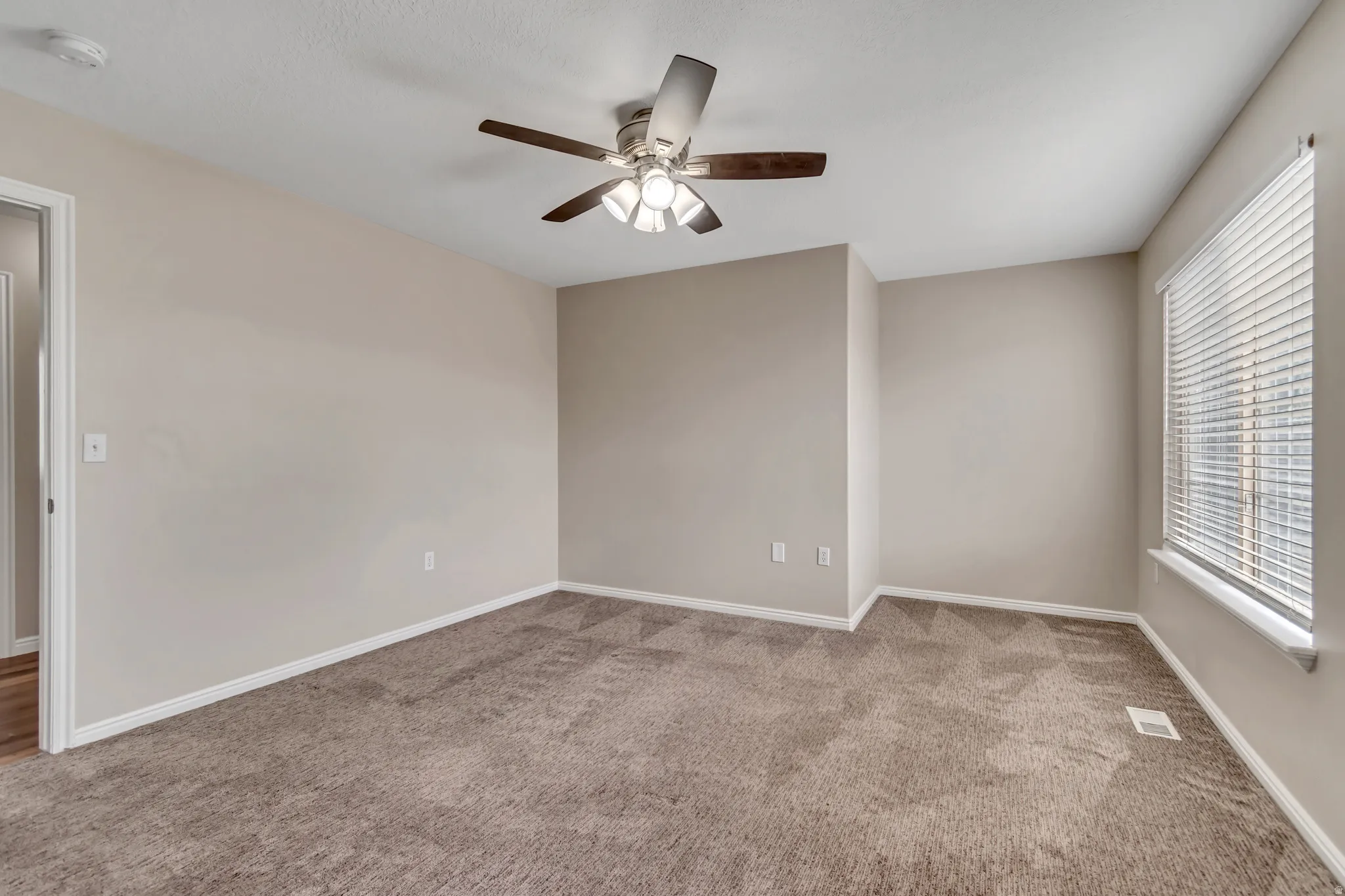 Spare room featuring carpet flooring, a ceiling fan, and a smoke detector