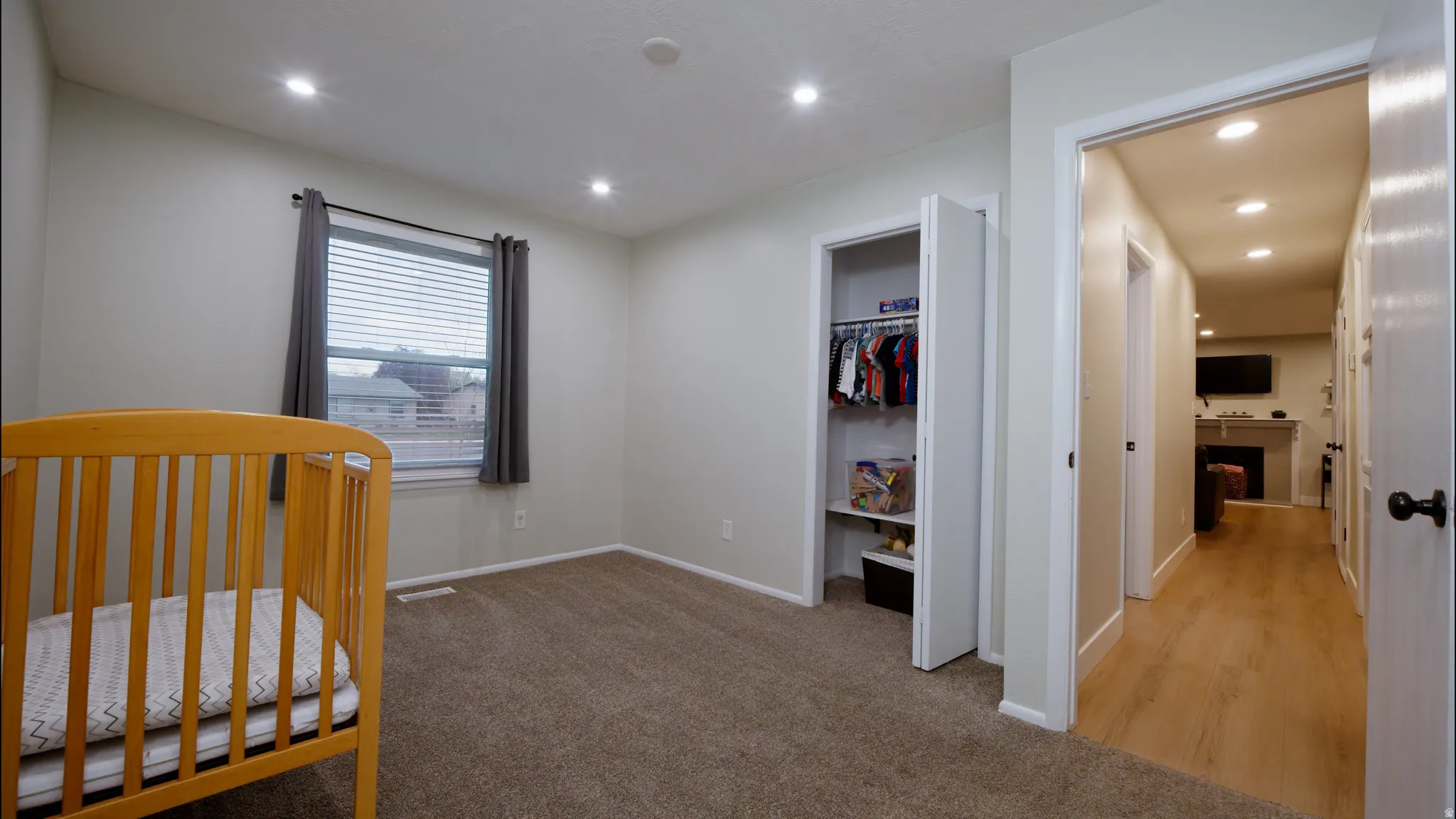 Bedroom with a fireplace, light colored carpet, recessed lighting, a walk in closet, and a nursery area