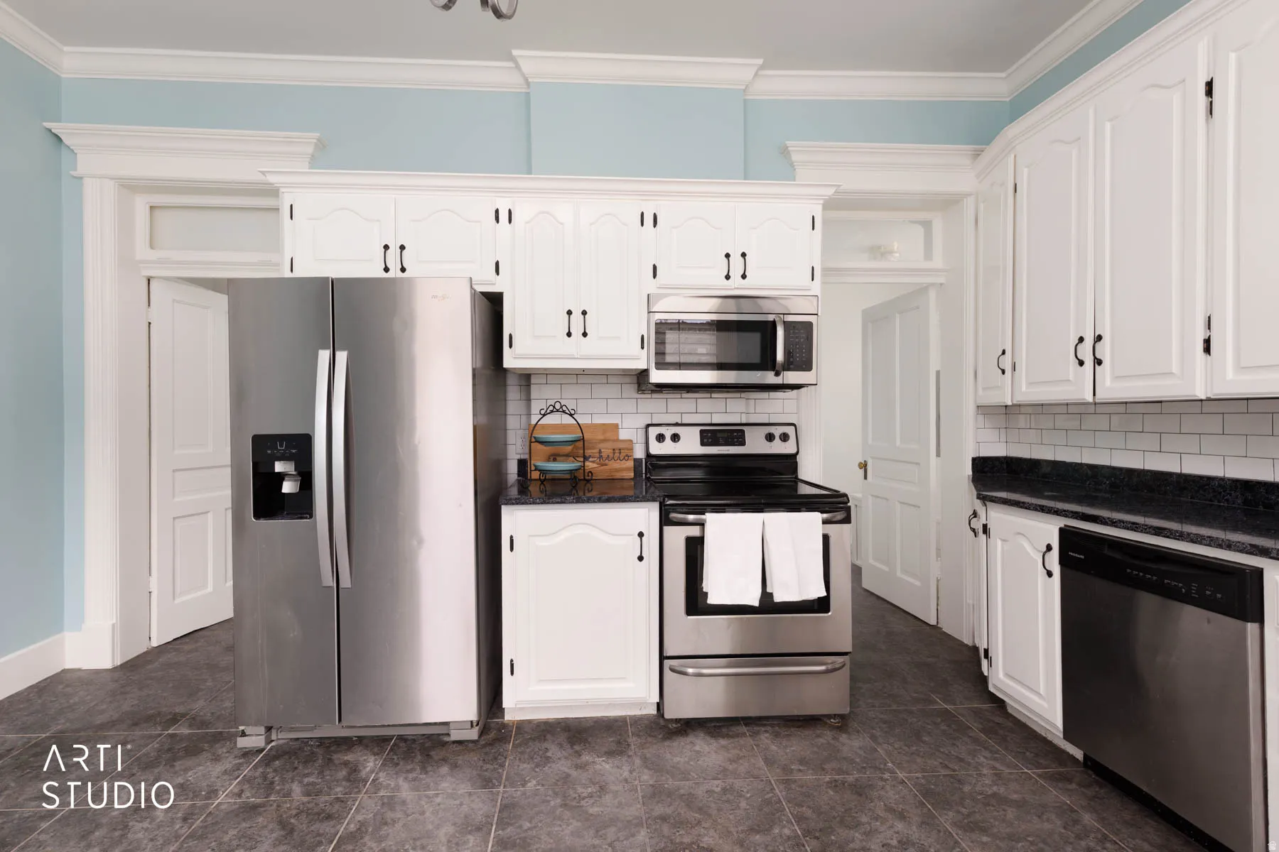 Kitchen with stainless steel appliances, white cabinets, crown molding, backsplash, and dark stone countertops